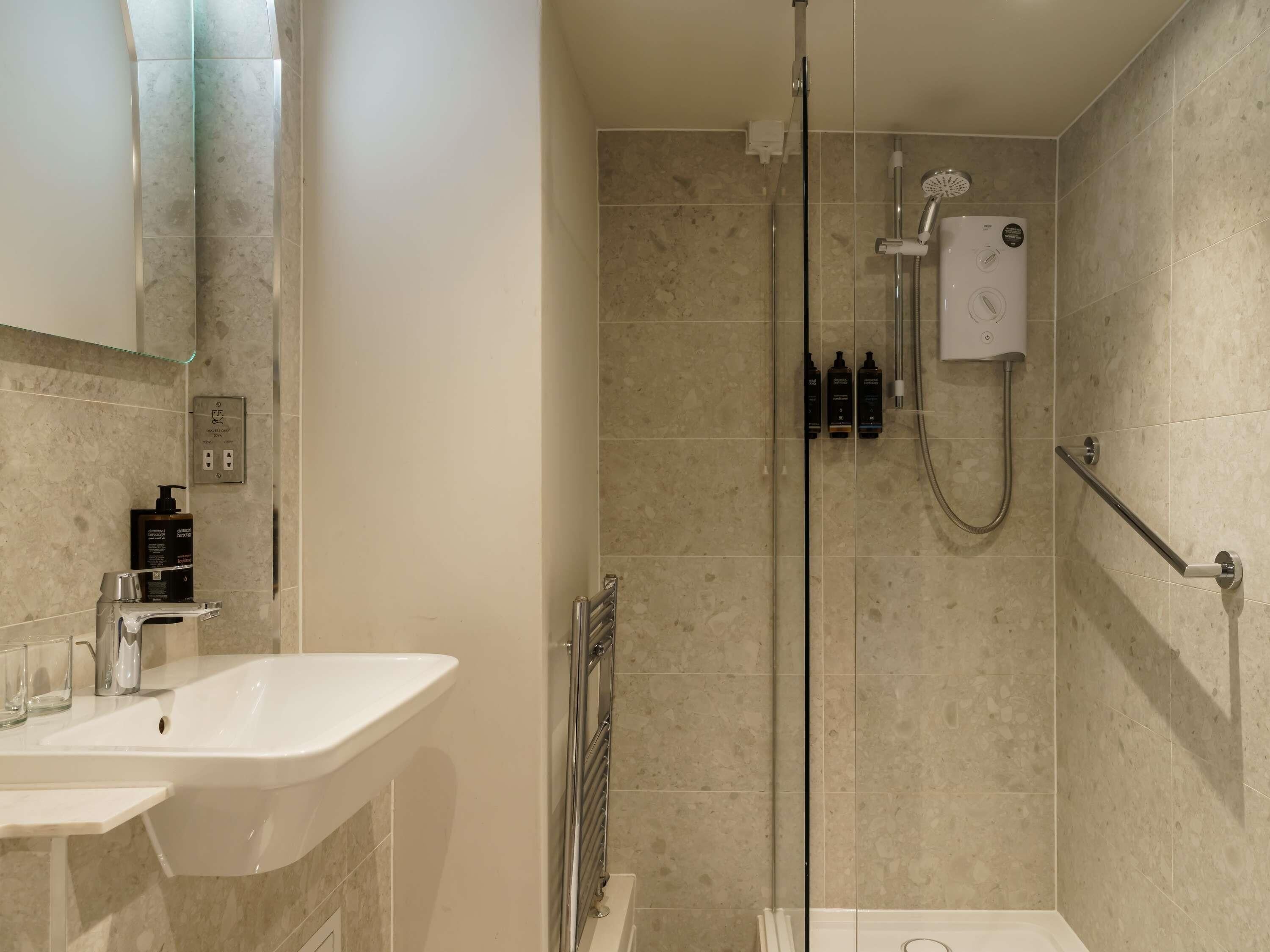 Un baño moderno con ducha vidriada, lavamanos blanco y ducha de mano.