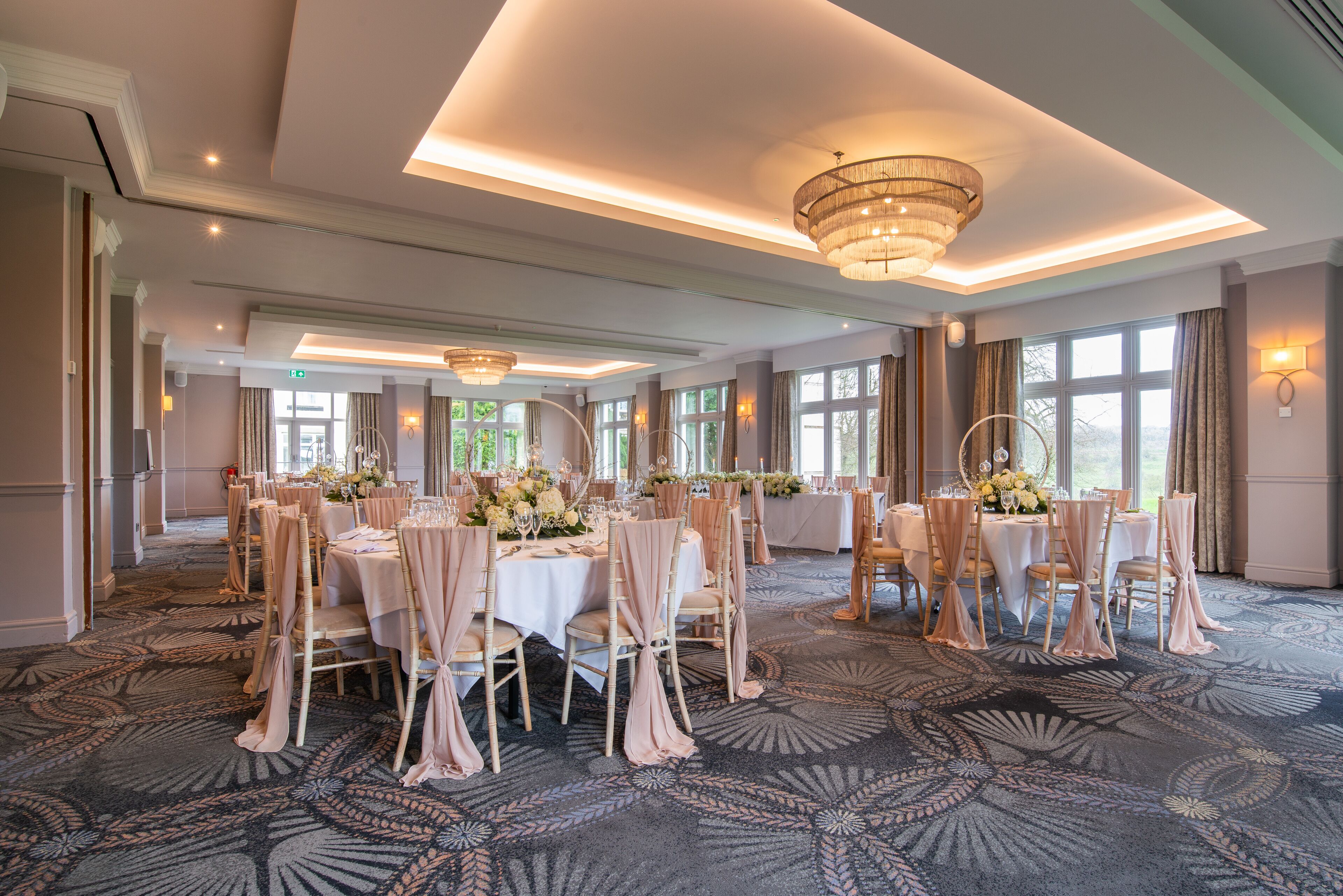 Une salle de banquet avec des tables rondes, des chaises et des centres de table floraux.