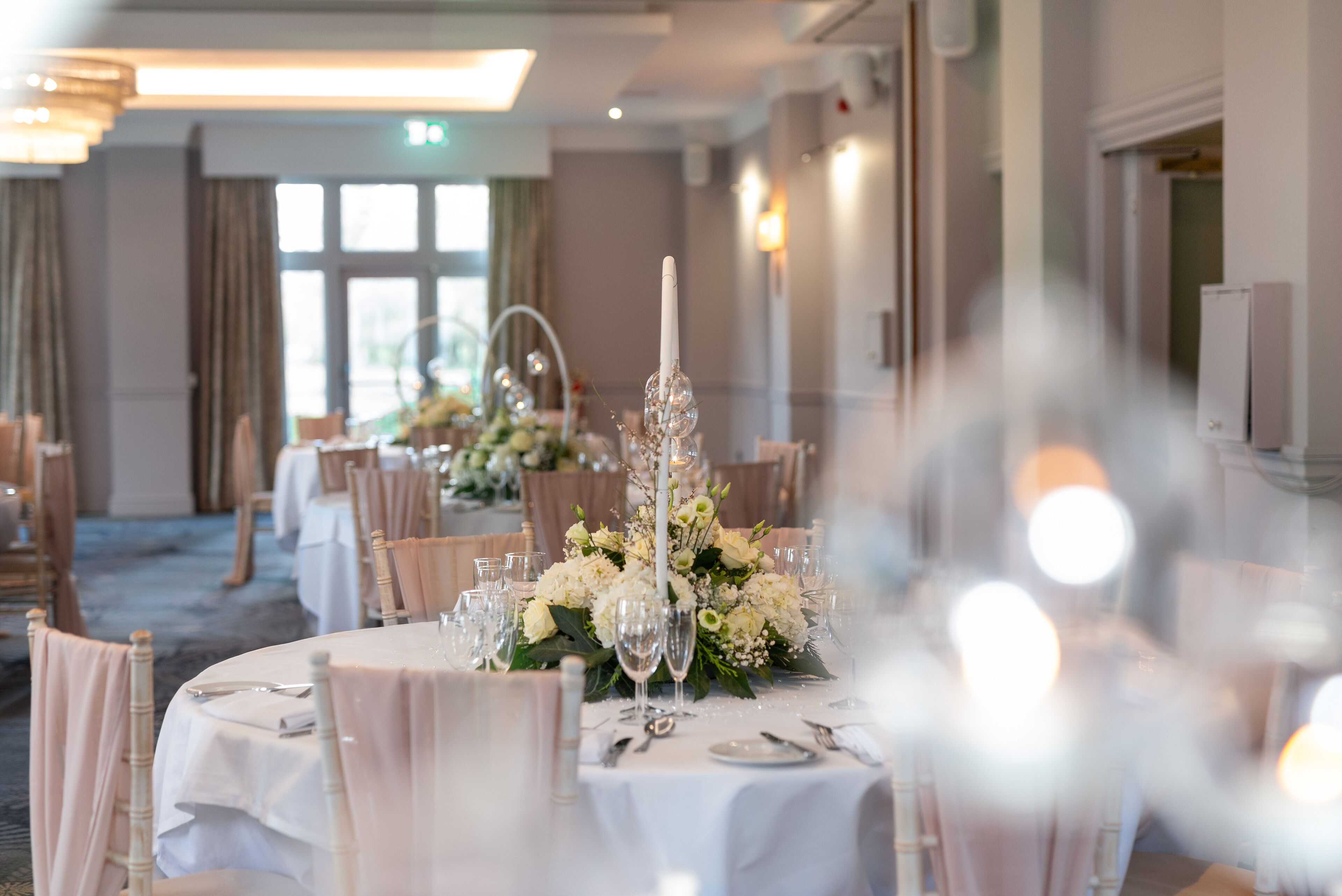 A banquet hall with round tables set for a formal event, featuring floral centerpieces and elegant table settings.