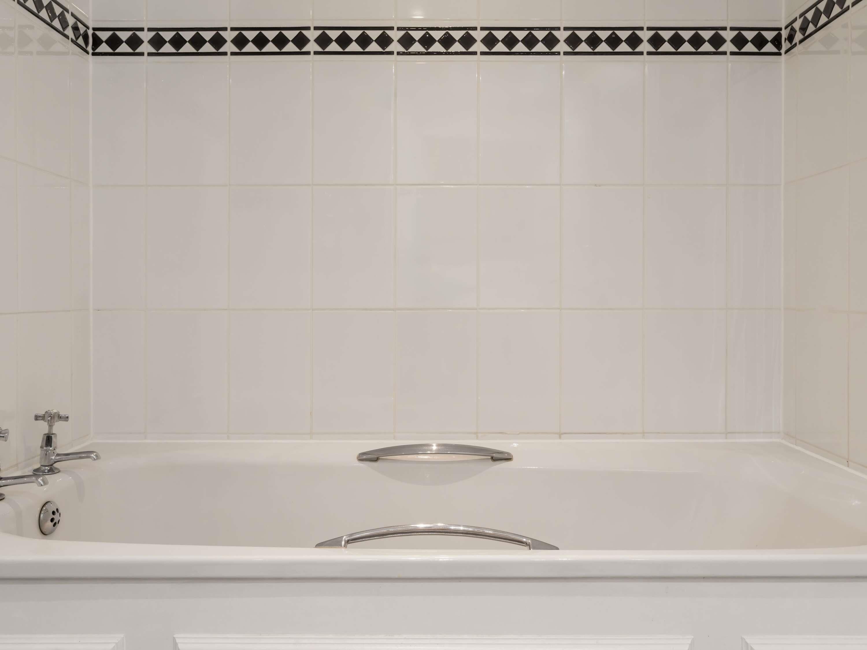Een badkamer met witte tegels, een badkuip en een douchehoek.