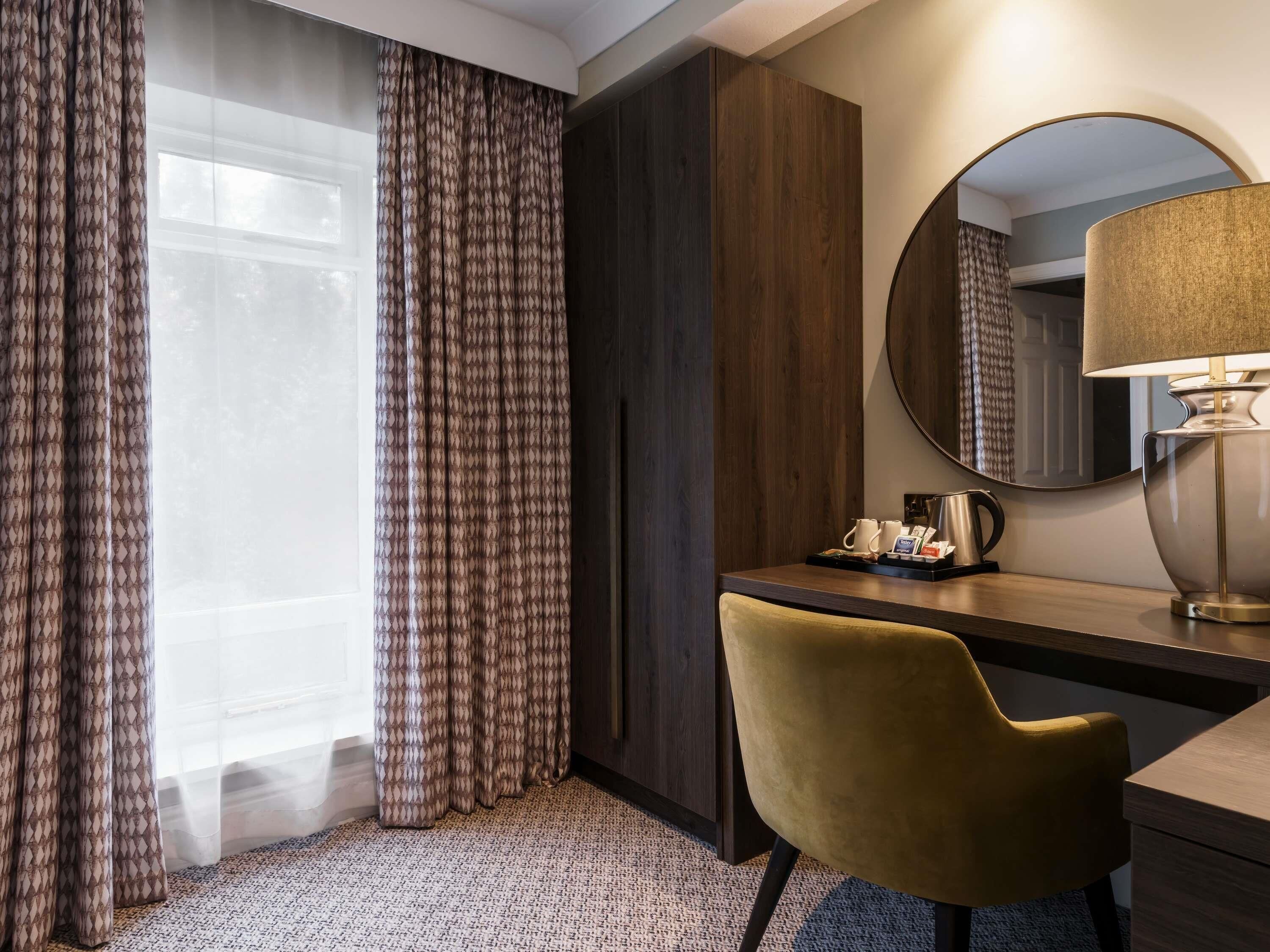 A hotel room with a desk, chair, and a large mirror.