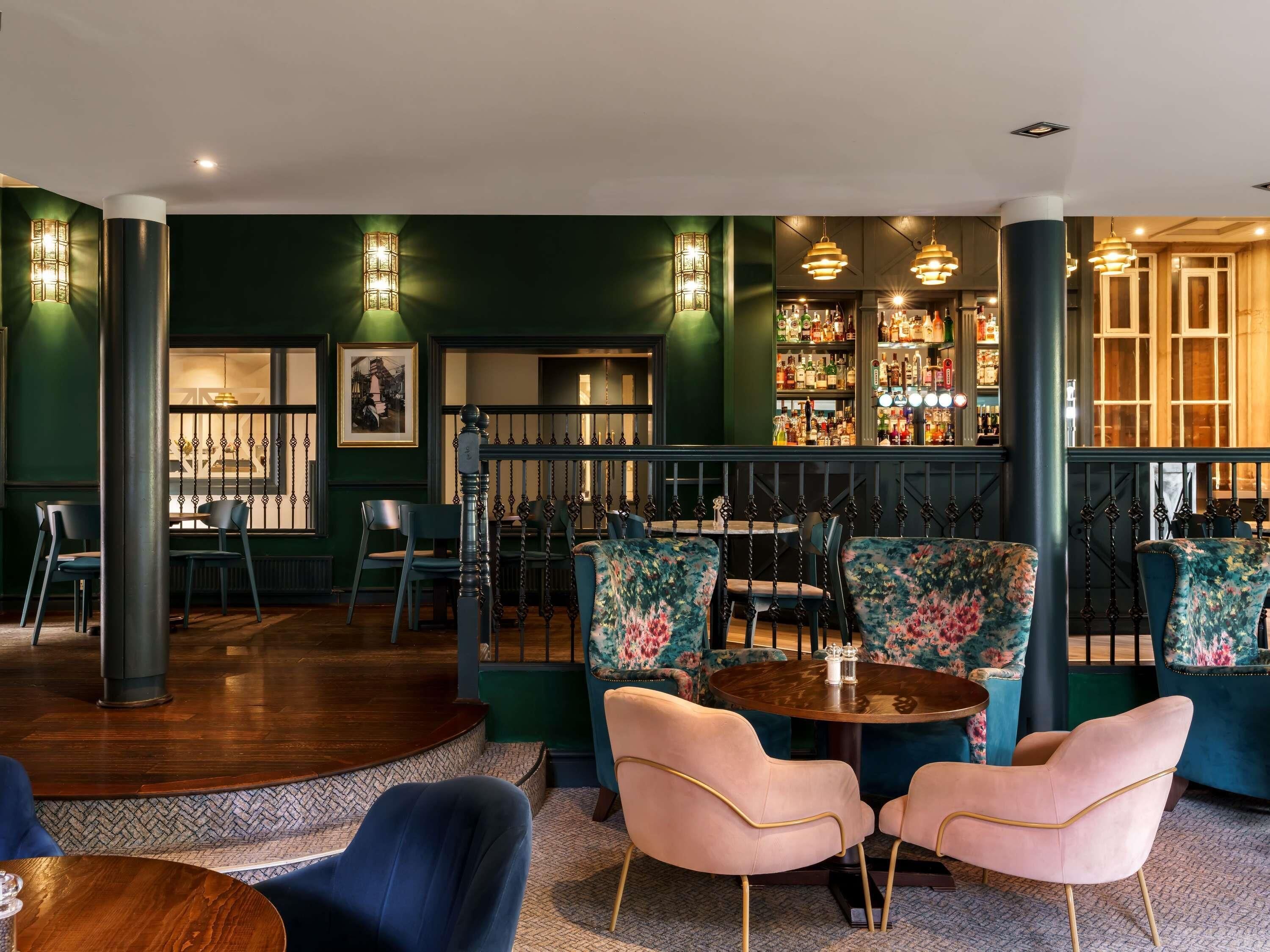 A bar area with a round table, floral upholstered chairs, and a bar stocked with bottles.