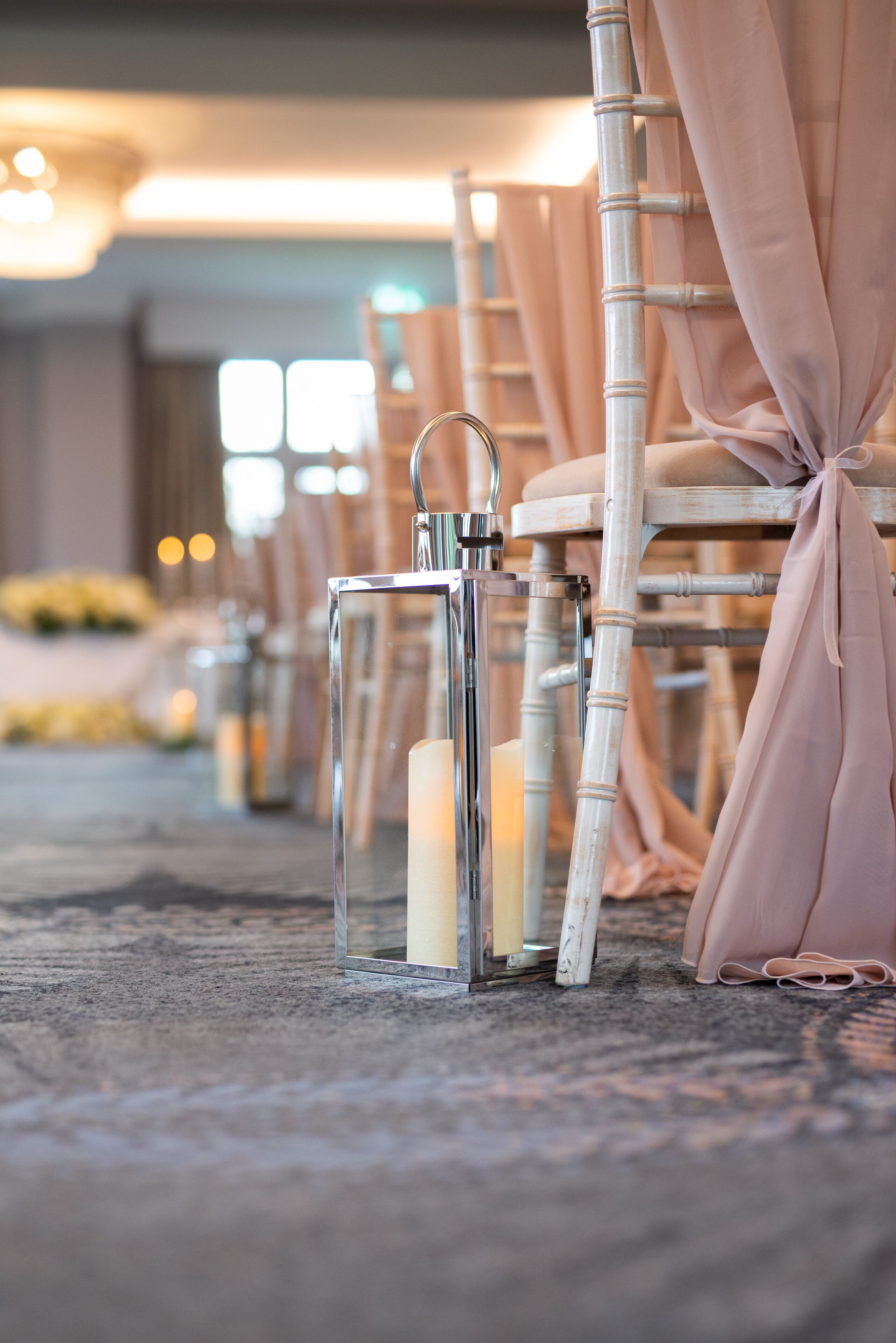 Rows of chairs with a candle in a glass holder, tied back with a fabric, in a well-lit indoor setting.