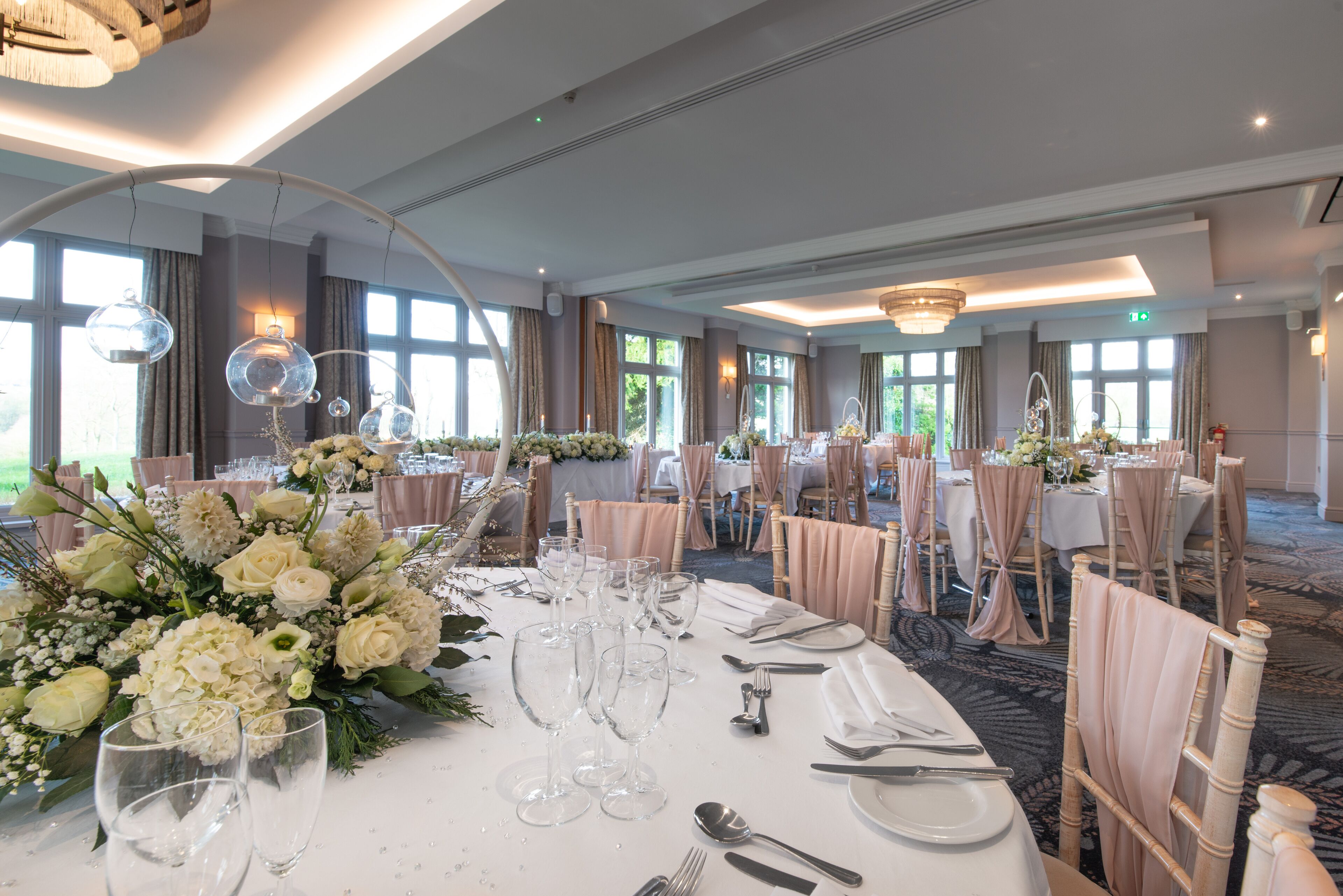 Un salón de banquetes con mesas redondas dispuestas para un evento formal, con centros de mesa florales y una elegante vajilla.