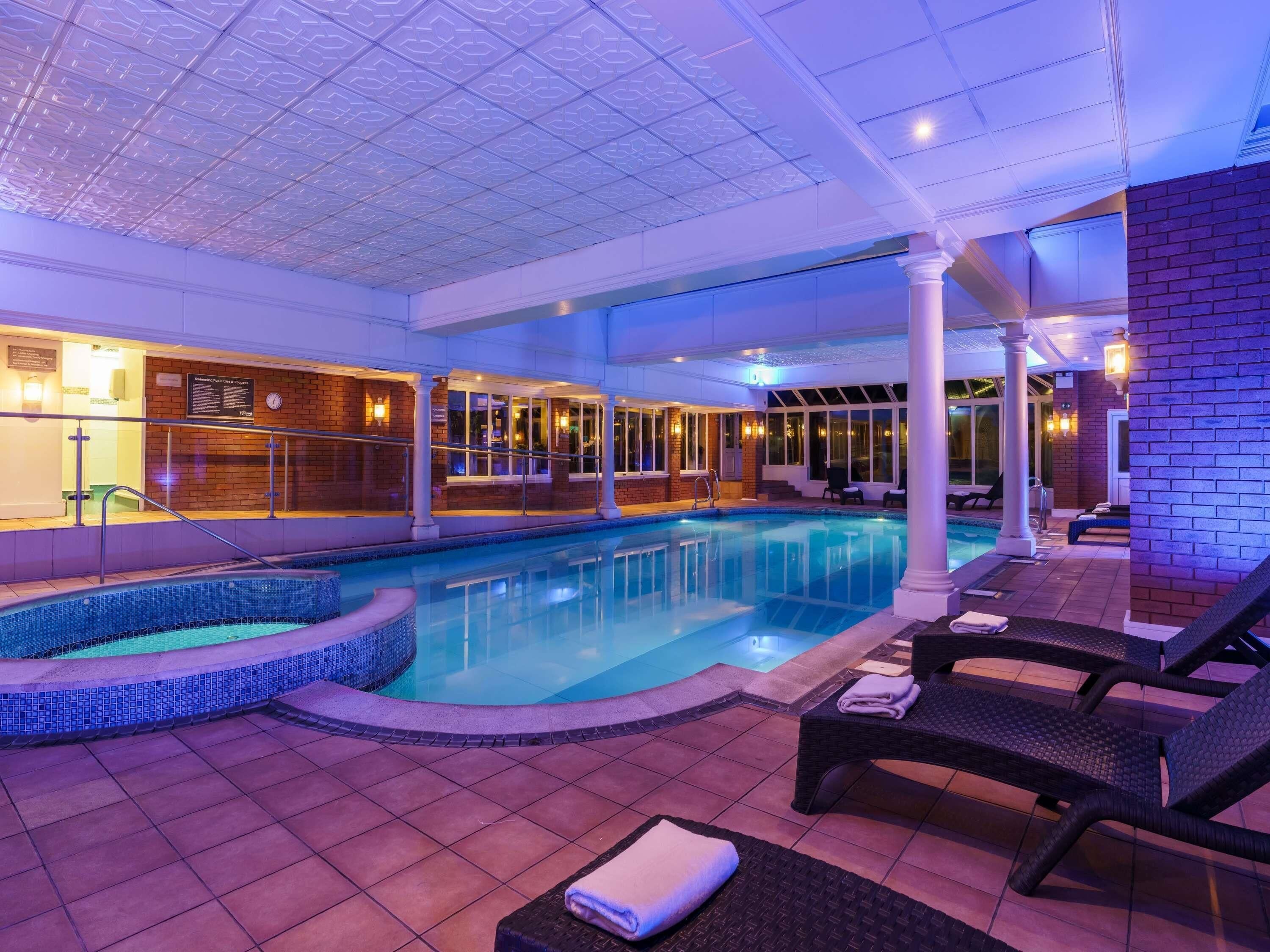 A pool area with a hot tub, lounge chairs, and a tiled floor.