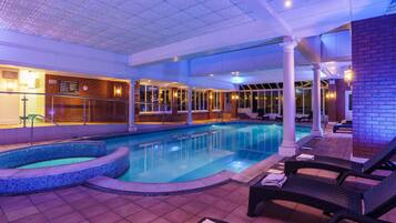 A pool area with a hot tub, lounge chairs, and a tiled floor.