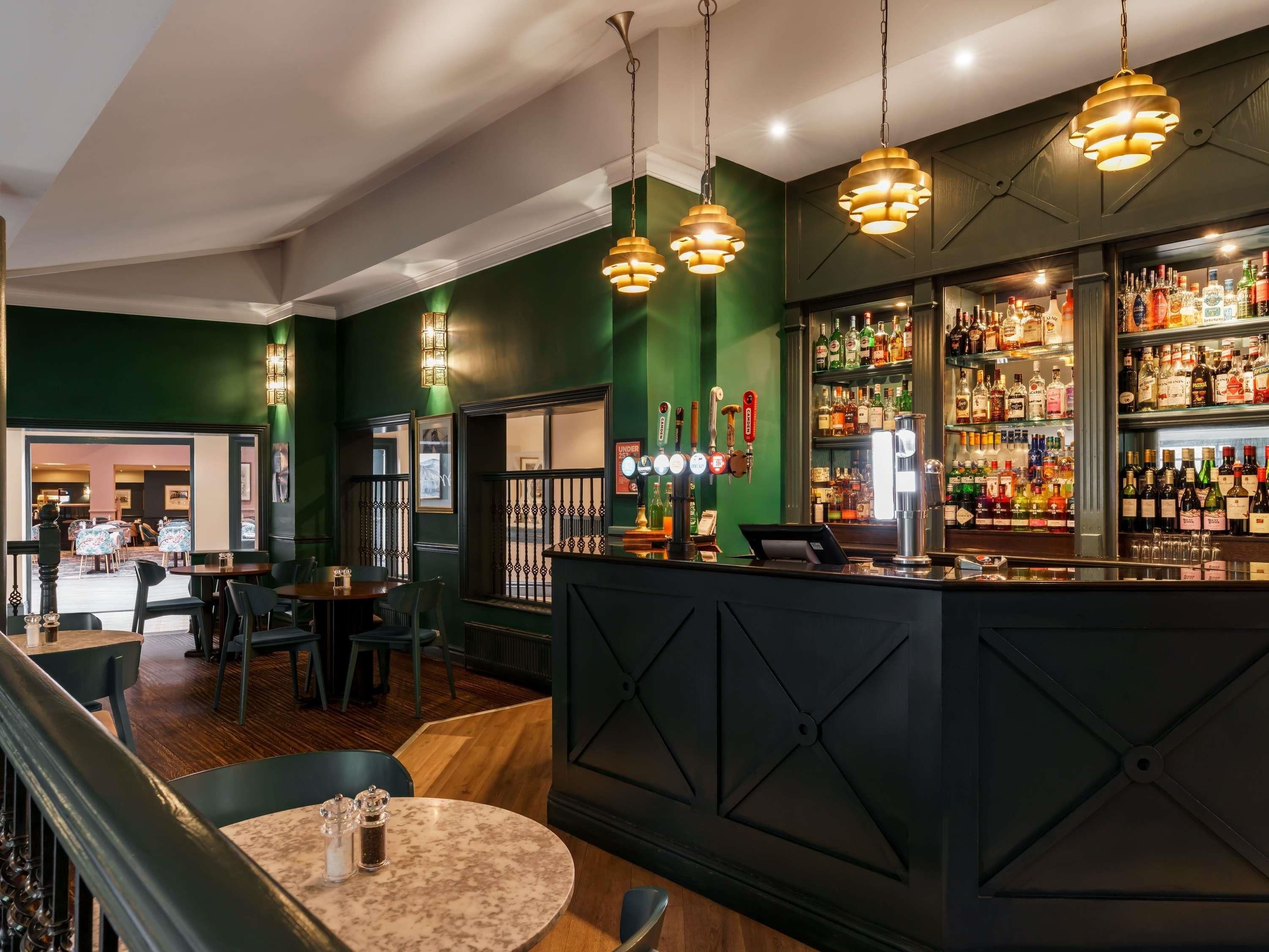 A bar area with a counter, bar stools, and a variety of bottles.