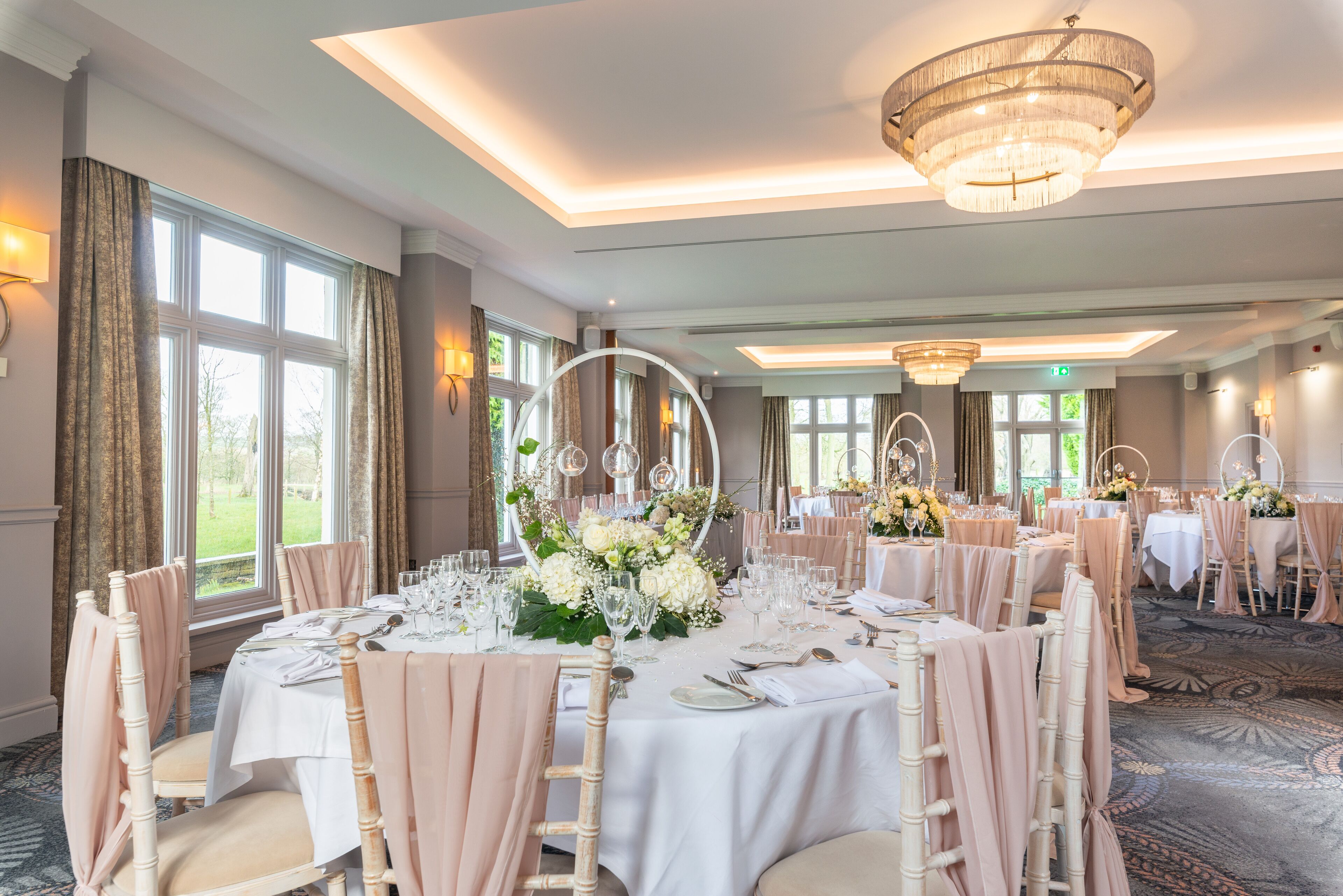 Un salón de banquetes con mesas redondas, candelabros y vistas al exterior.