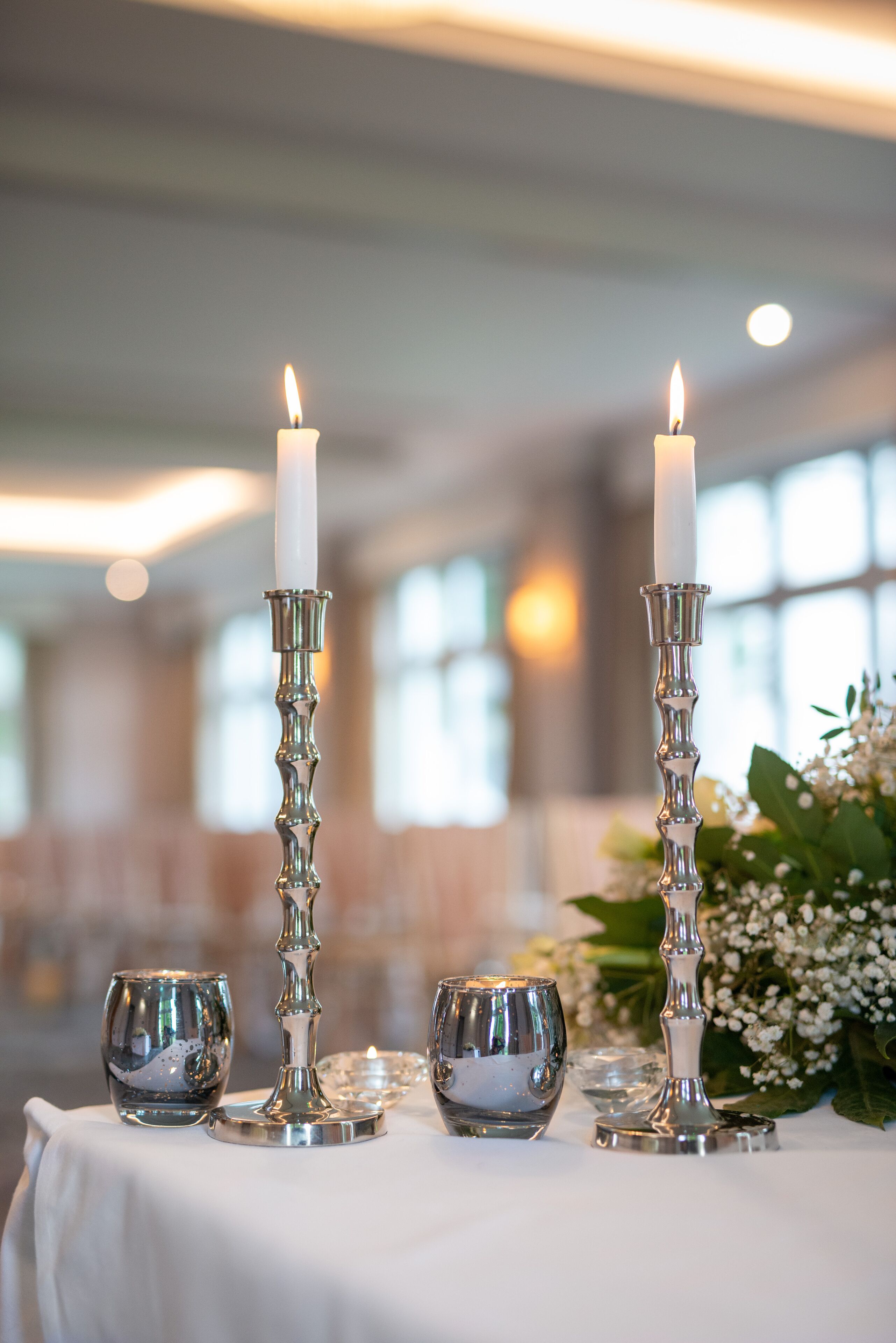 A table with two lit candles, two glass candle holders, and a floral arrangement.