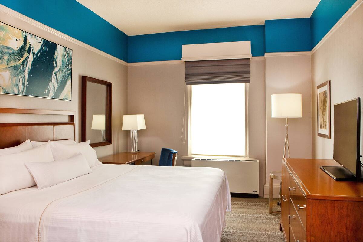 A hotel room with a large bed, a desk with a chair, a television, and a window with a view.