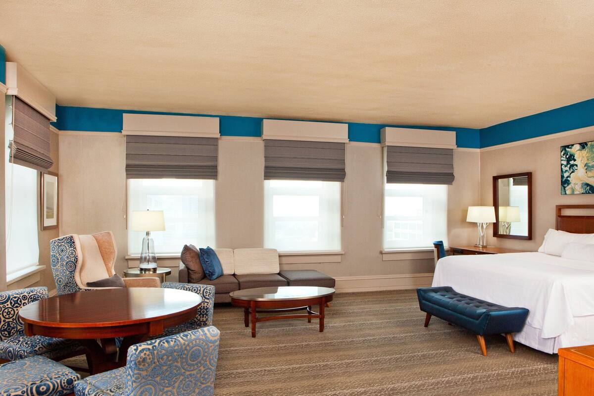 A hotel room with a bed, two sofas, a round table, and a bench.