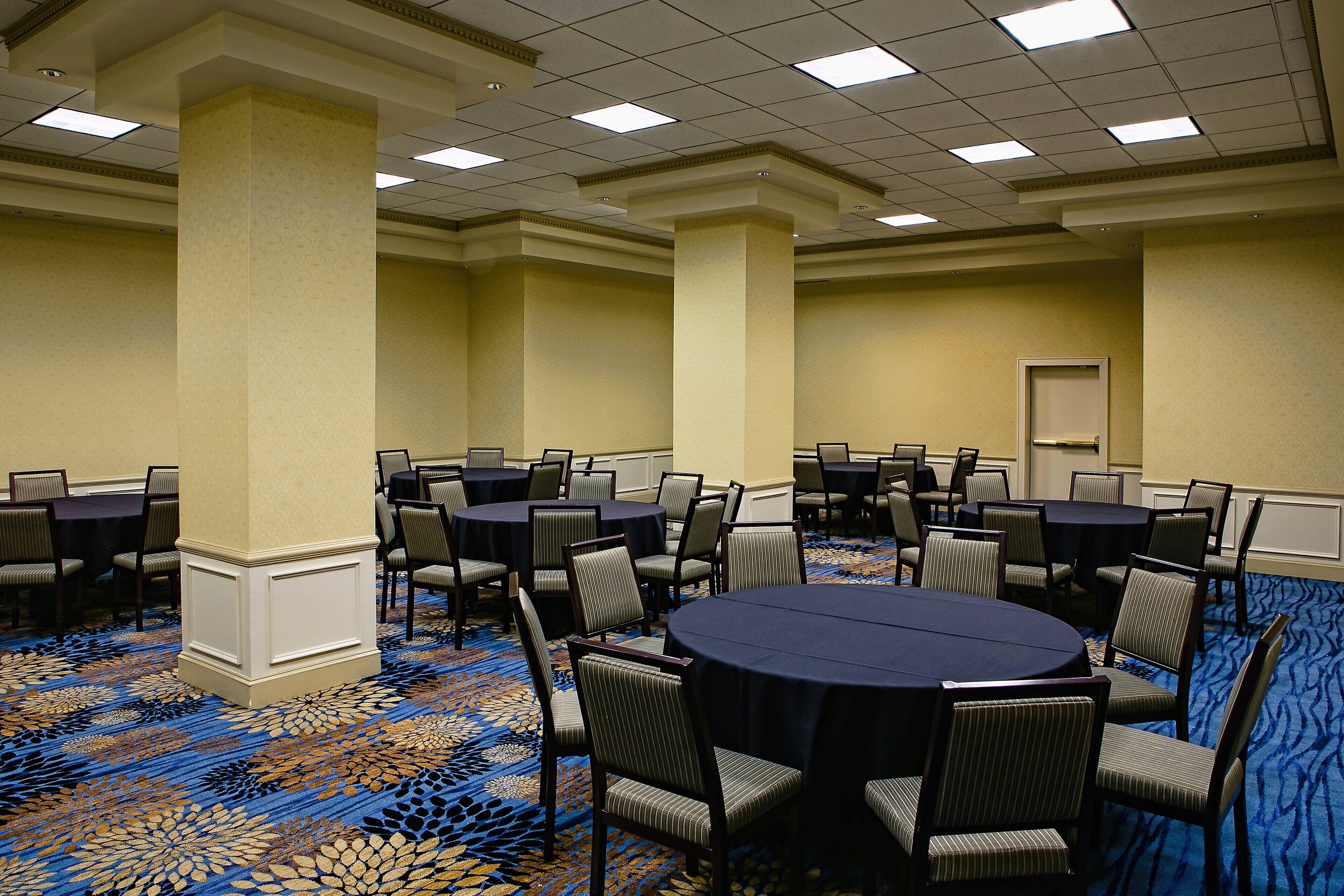 A conference room with round tables and chairs, carpeted floor, and a door in the background.