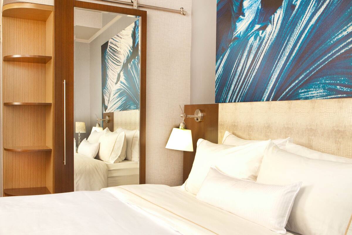 A hotel room with a bed, a nightstand, a lamp, a mirror, and a wall with a large abstract painting.