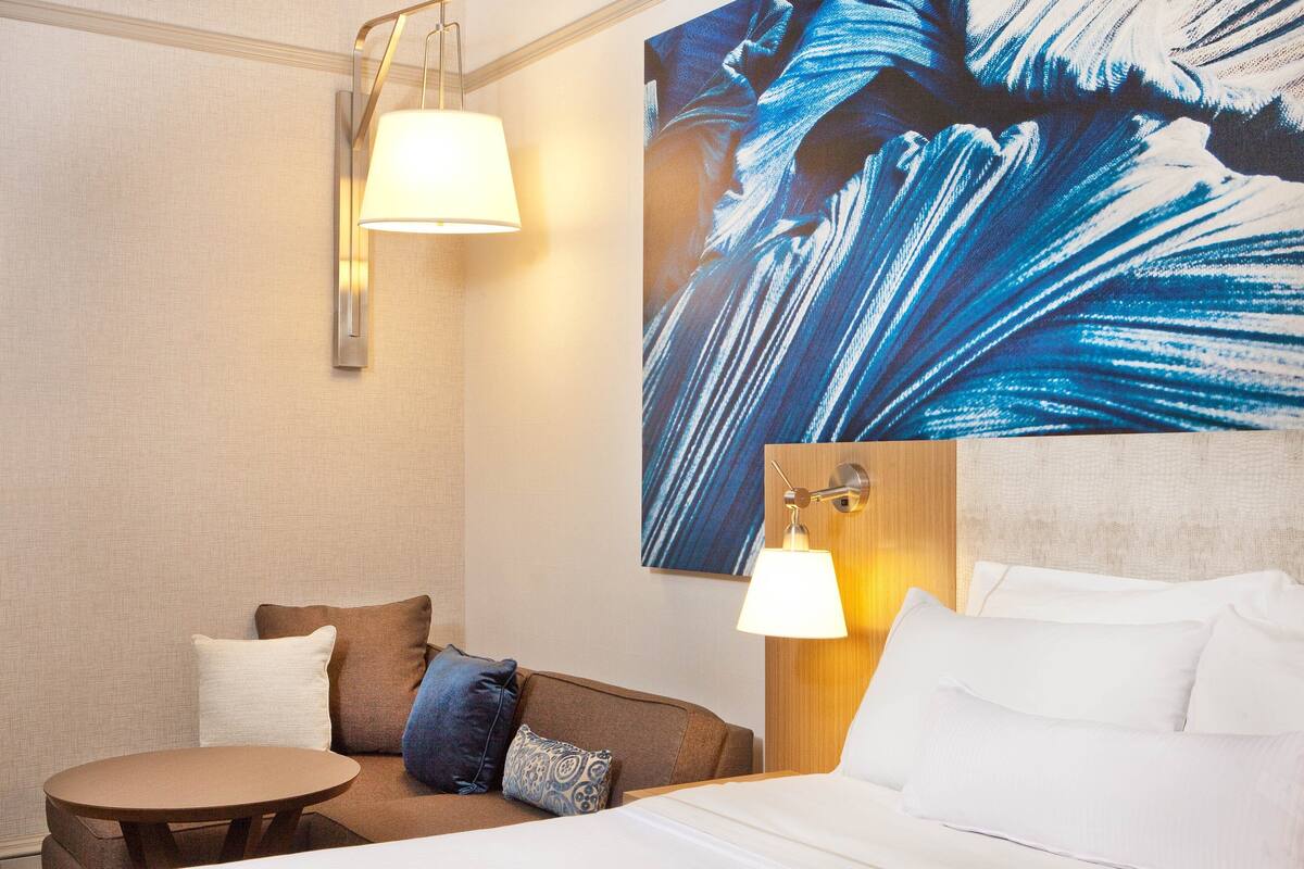 A hotel room with a bed, a sofa, a small table, and a wall-mounted lamp.