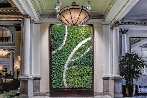 A lobby with a large vertical garden, marble columns, and a chandelier.