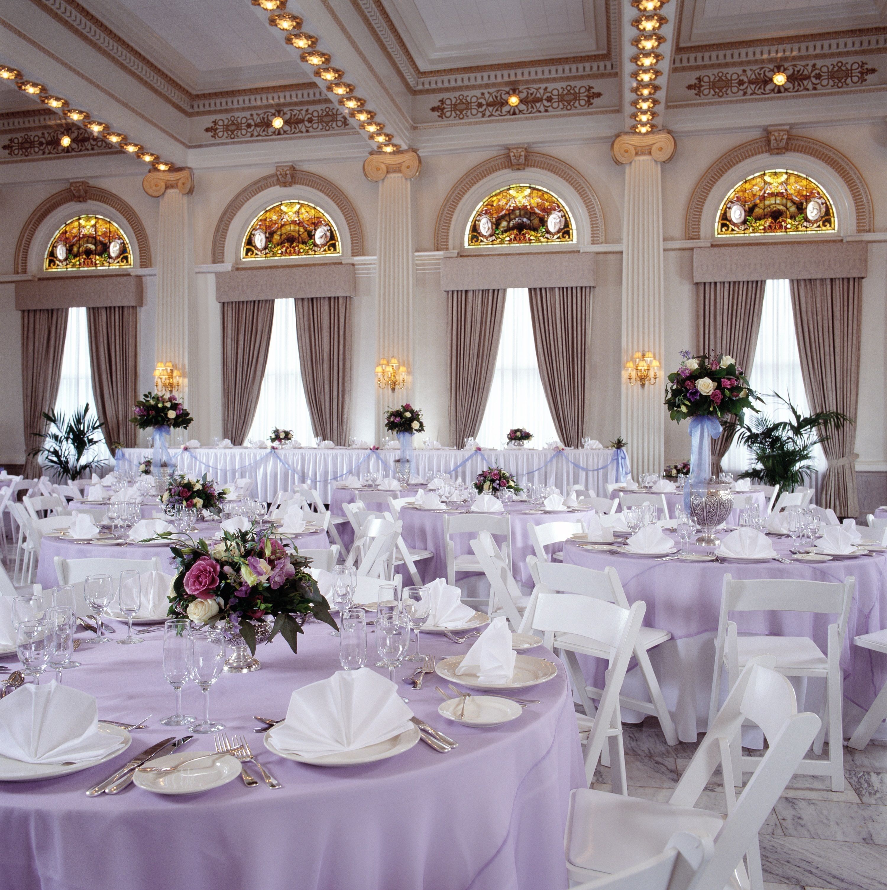 A banquet hall with round tables covered in white tablecloths, white chairs, and floral centerpieces.