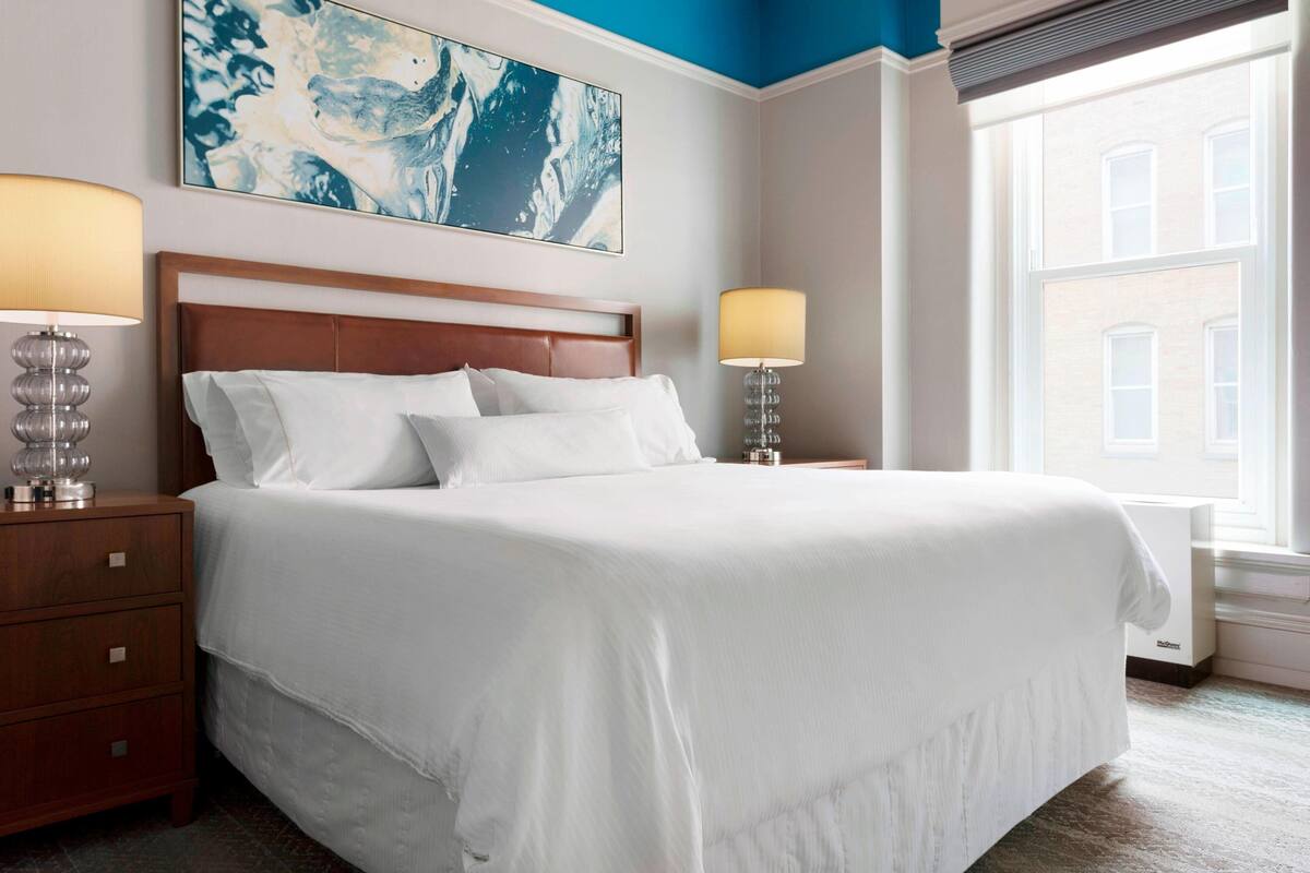 A neatly made bed with white linens, a wooden headboard, and two bedside lamps.