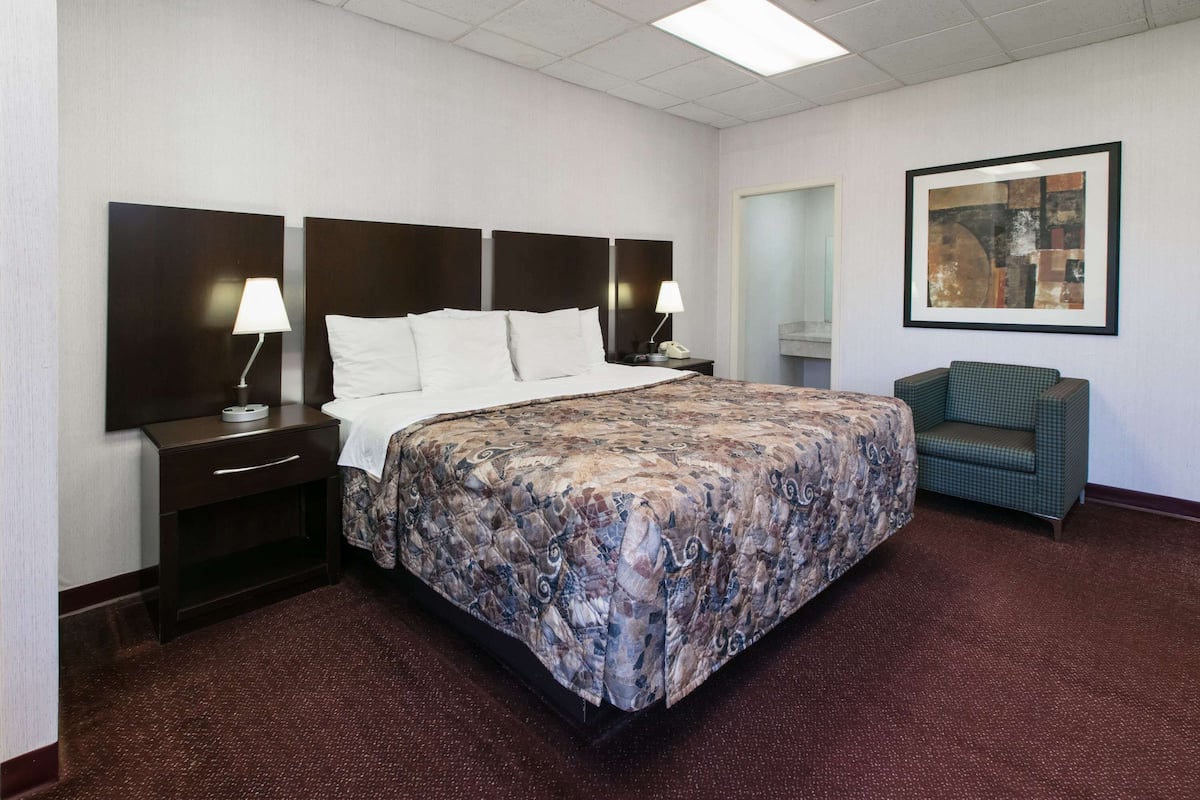 A hotel room with a large bed, two bedside tables with lamps, a chair, and a framed artwork on the wall.