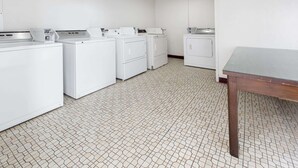 Un área de lavandería con cuatro lavadoras blancas y una mesa.