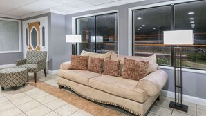 Una sala de estar con un sofá color beige, un sillón estampado y un reposapiés.