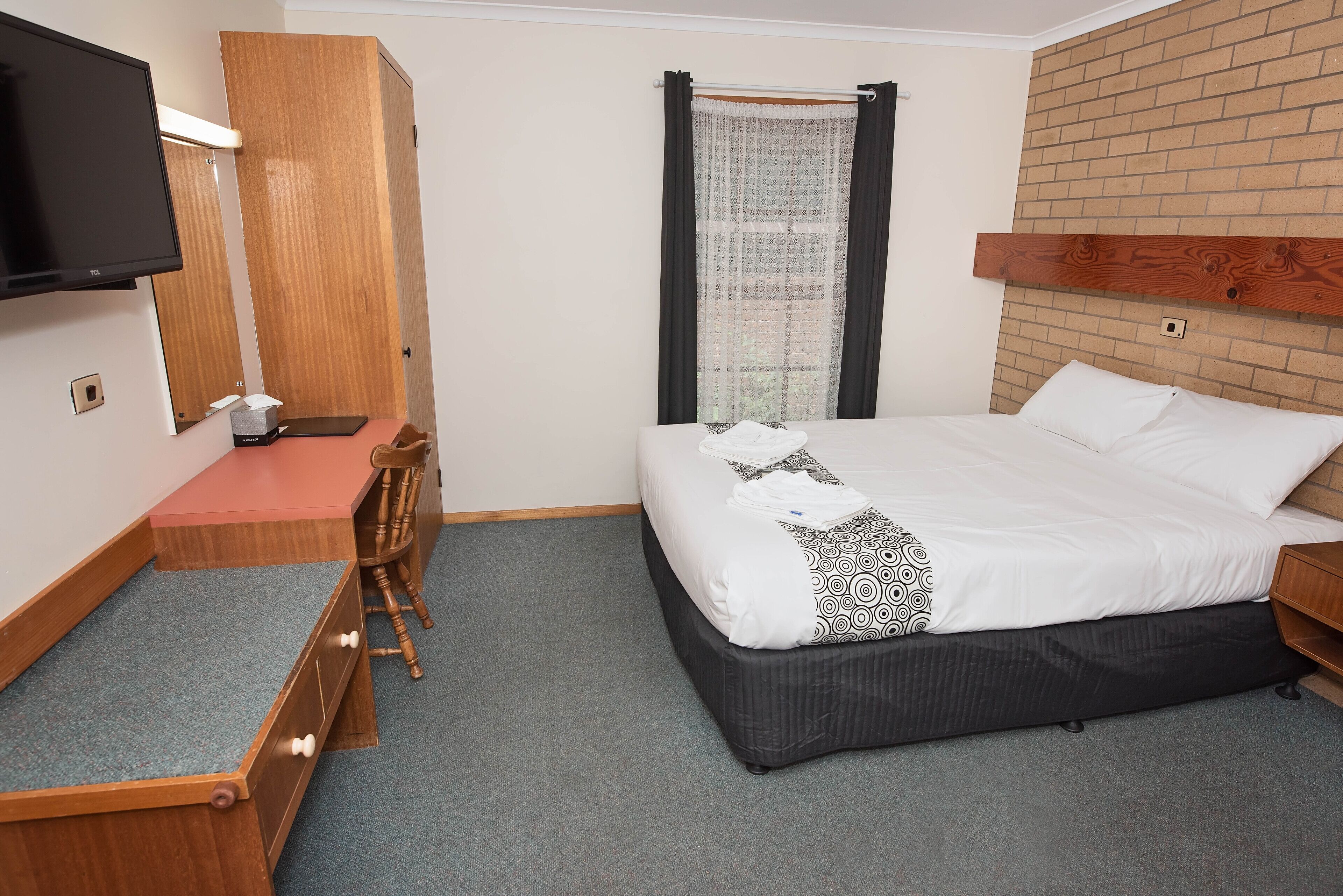 Habitación de hotel con cama, escritorio, silla, televisor y ventana con cortinas.