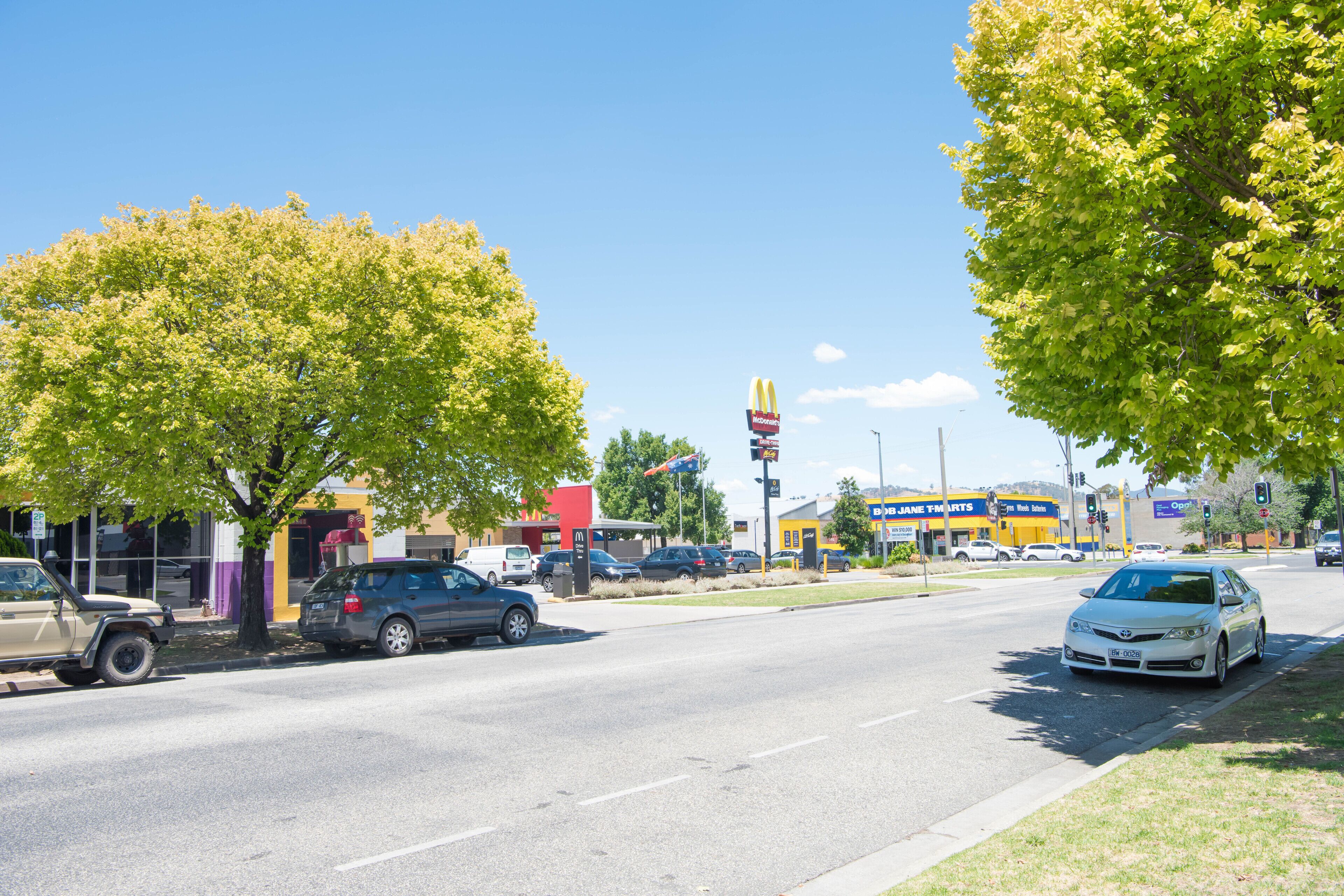 Straatbeeld met geparkeerde auto's, een McDonald's bord en een winkel van Jane's T-shirts.