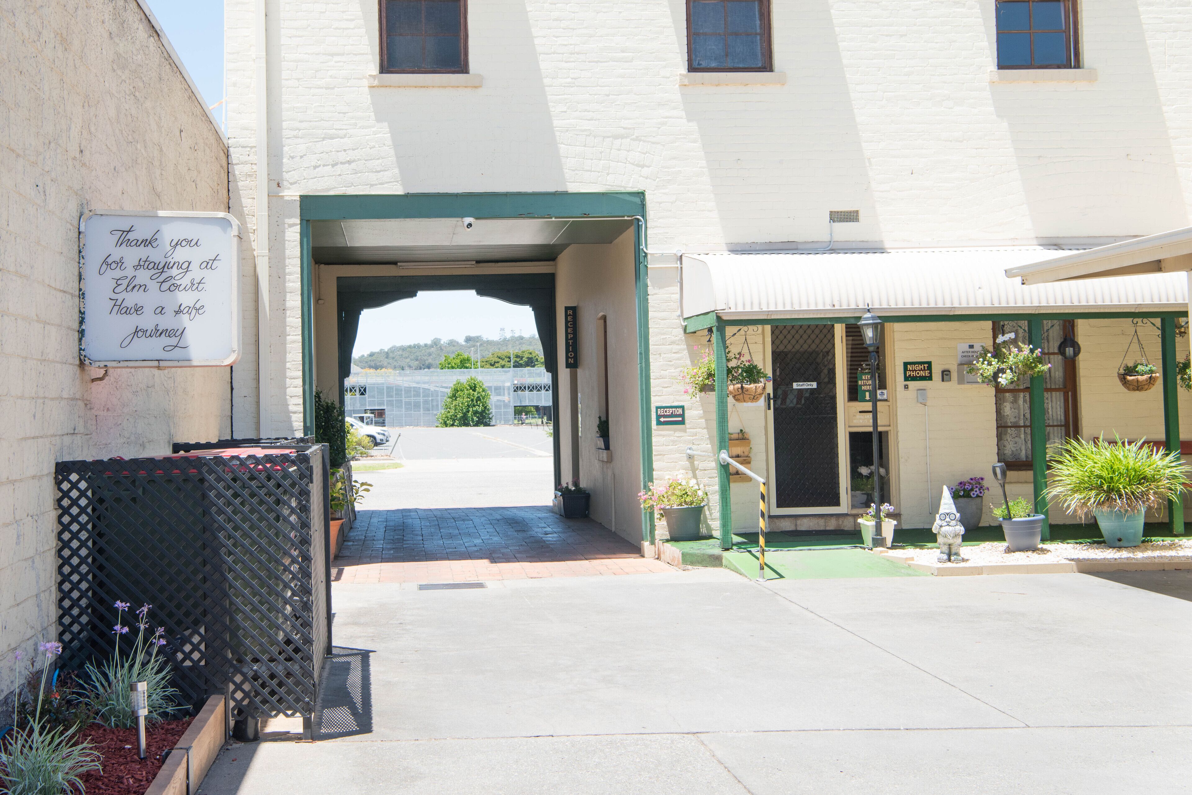 A hotel entrance with a sign thanking guests for their stay, a green awning, and potted plants outside.