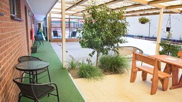 A covered patio area with a brick wall, green artificial turf, and wooden furniture.