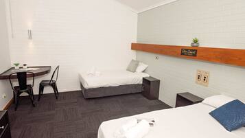 A hotel room with a bed, a desk with a chair, a small sink, and a wooden shelf with a sign.