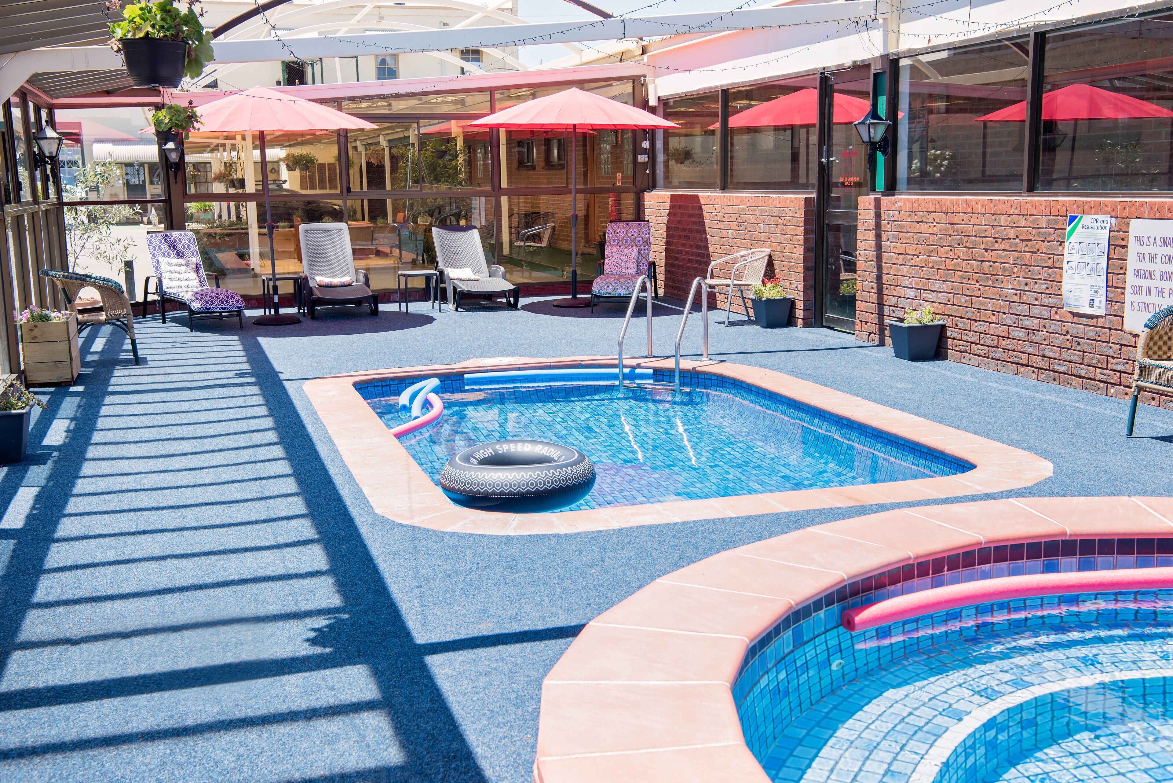Un área de piscina en la azotea con sillones de descanso, sombrillas y una piscina pequeña con un flotador con forma de neumático.