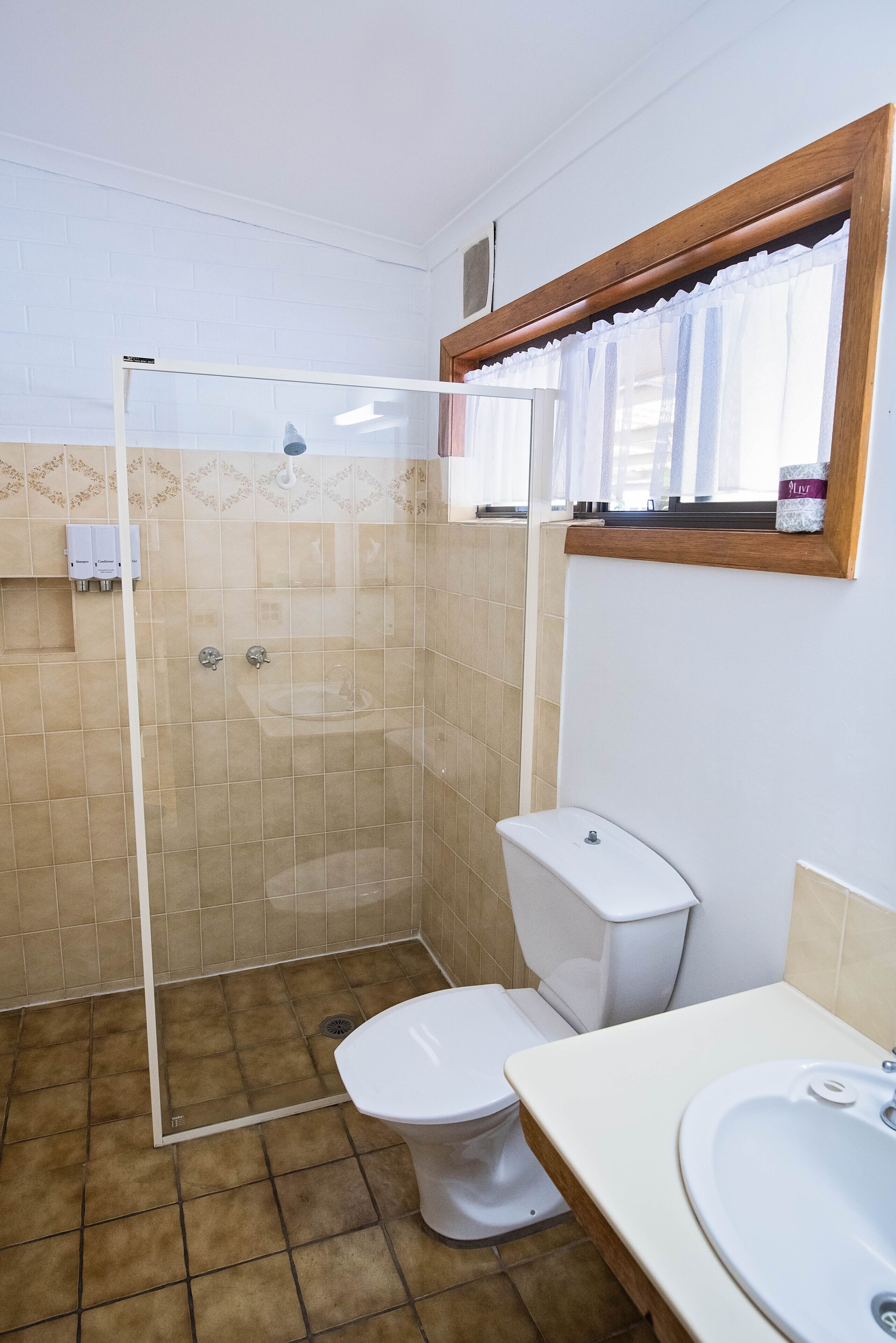 A bathroom with a shower, toilet, sink, and a window with a curtain.