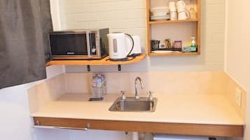 Eine kompakte Küchenzeile mit Mikrowelle, Kaffeemaschine und kleinem Kühlschrank.
