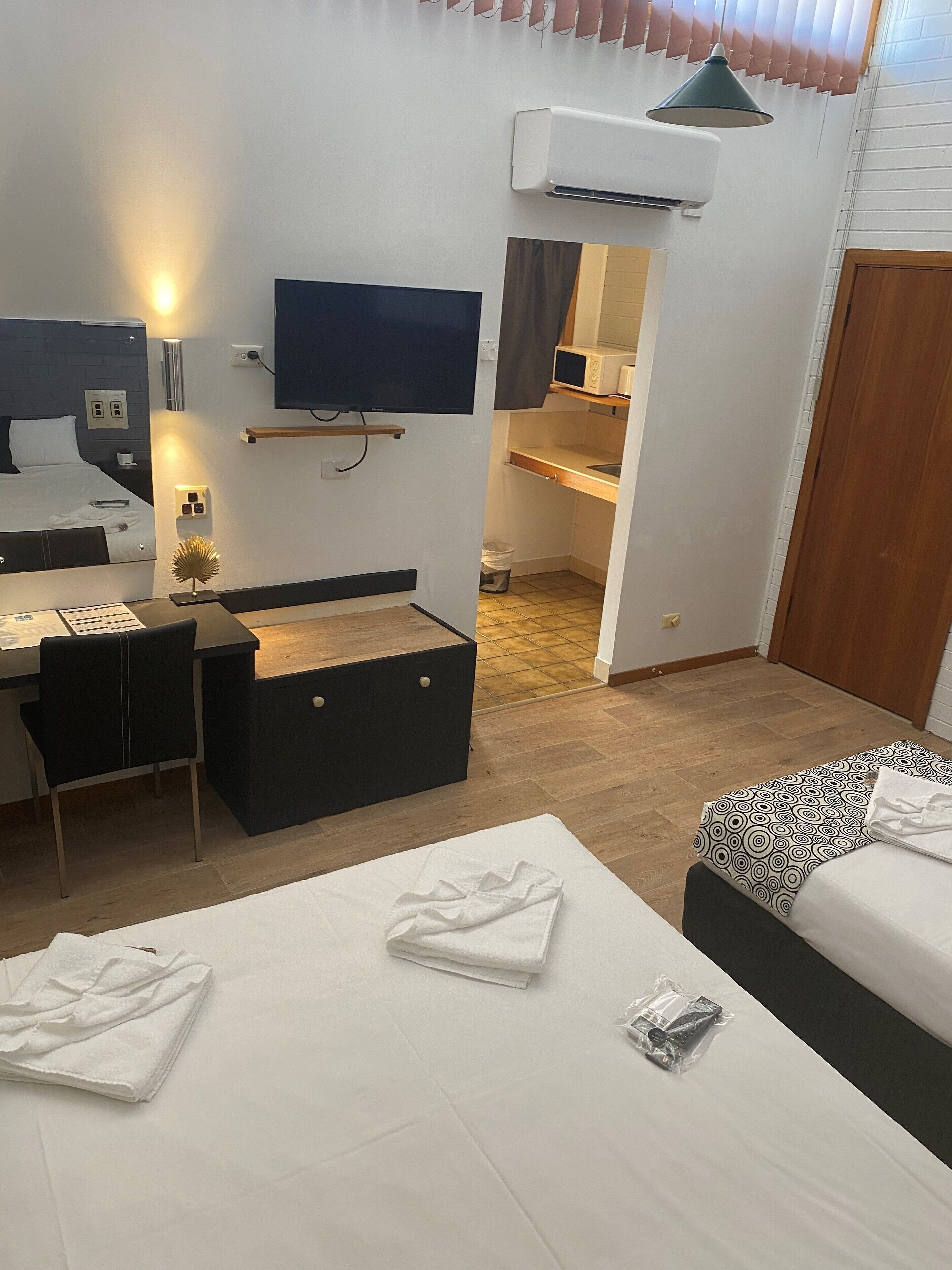 Ein kleines Hotelzimmer mit einem Bett, einem Schreibtisch, einem Stuhl, einem Fernseher, einer Mikrowelle und einer Klimaanlage.