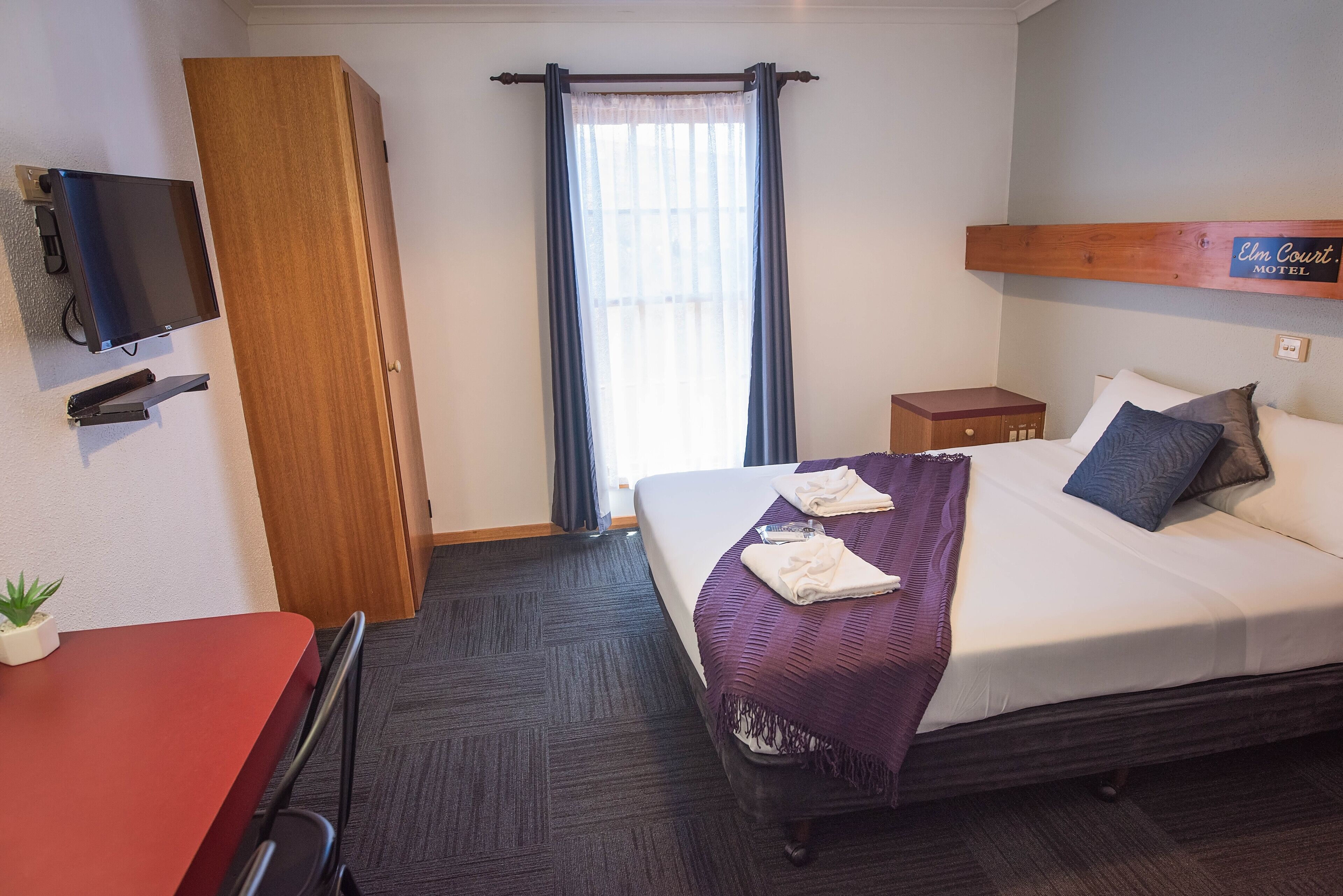 A hotel room with a bed, a desk, a TV, and a window with curtains.