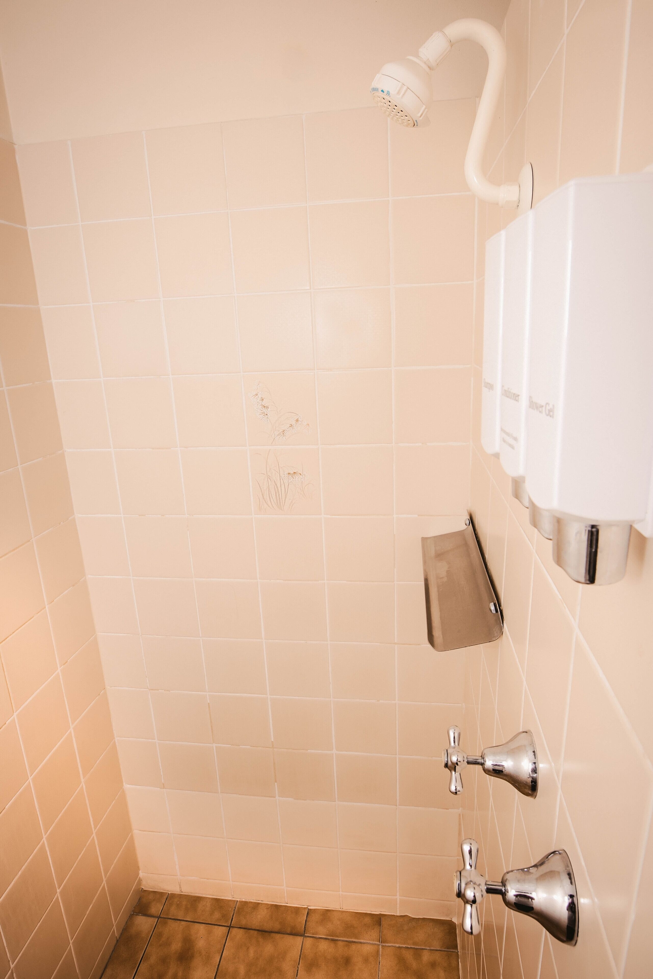 Een badkamer met beige tegels, een douchekop, een zeepdispenser en een handdoekhouder.