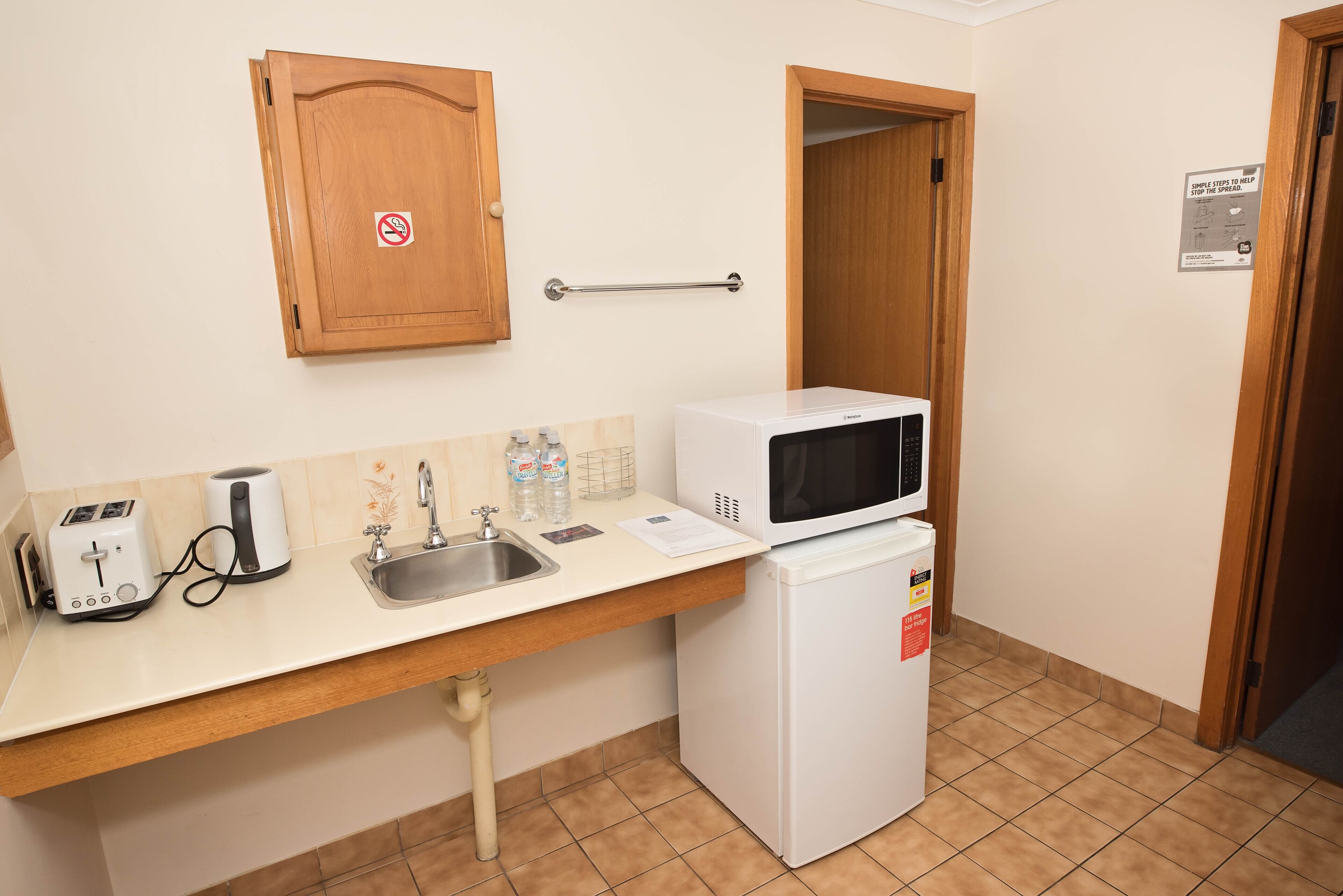A small kitchenette with a microwave, toaster, sink, and wooden cabinet.