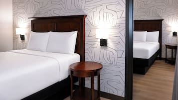 Une chambre d’hôtel avec deux lits, une petite table d’appoint ronde en bois et un papier peint à motifs.