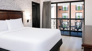 Ein Hotelzimmer mit einem großen Bett, einem hölzernen Kopfteil, einem Balkon mit Metallstühlen und einem Backsteinhaus im Hintergrund.