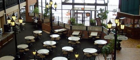 An indoor patio area with round tables and chairs, surrounded by brick walls and glass railings.