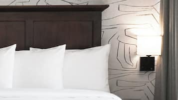 A bed with white bedding, a dark wooden headboard, and a wall with a geometric pattern.