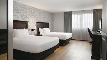 A hotel room with two beds, a desk, and a large window with curtains.