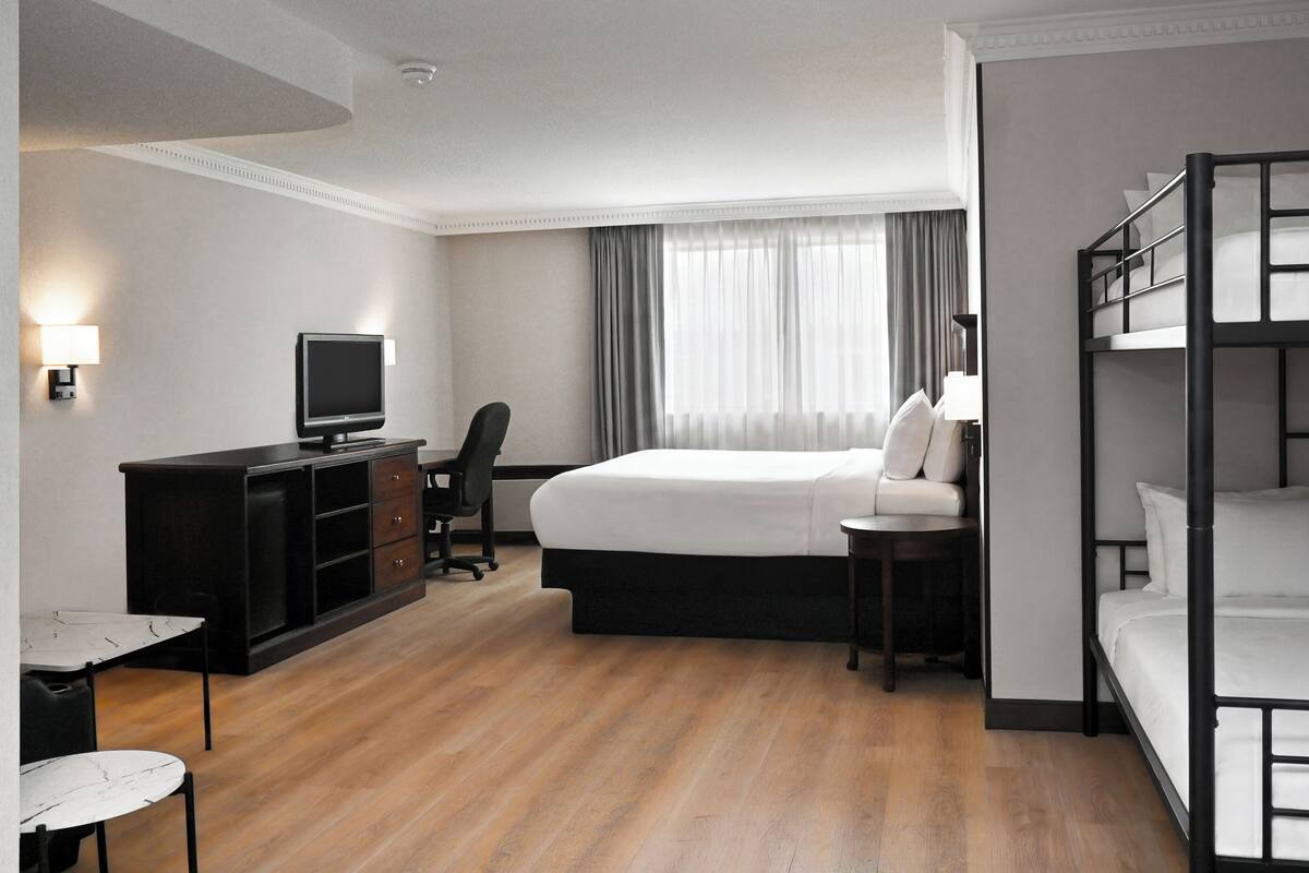 A hotel room with a bed, a desk with a computer, a television, and a bunk bed.