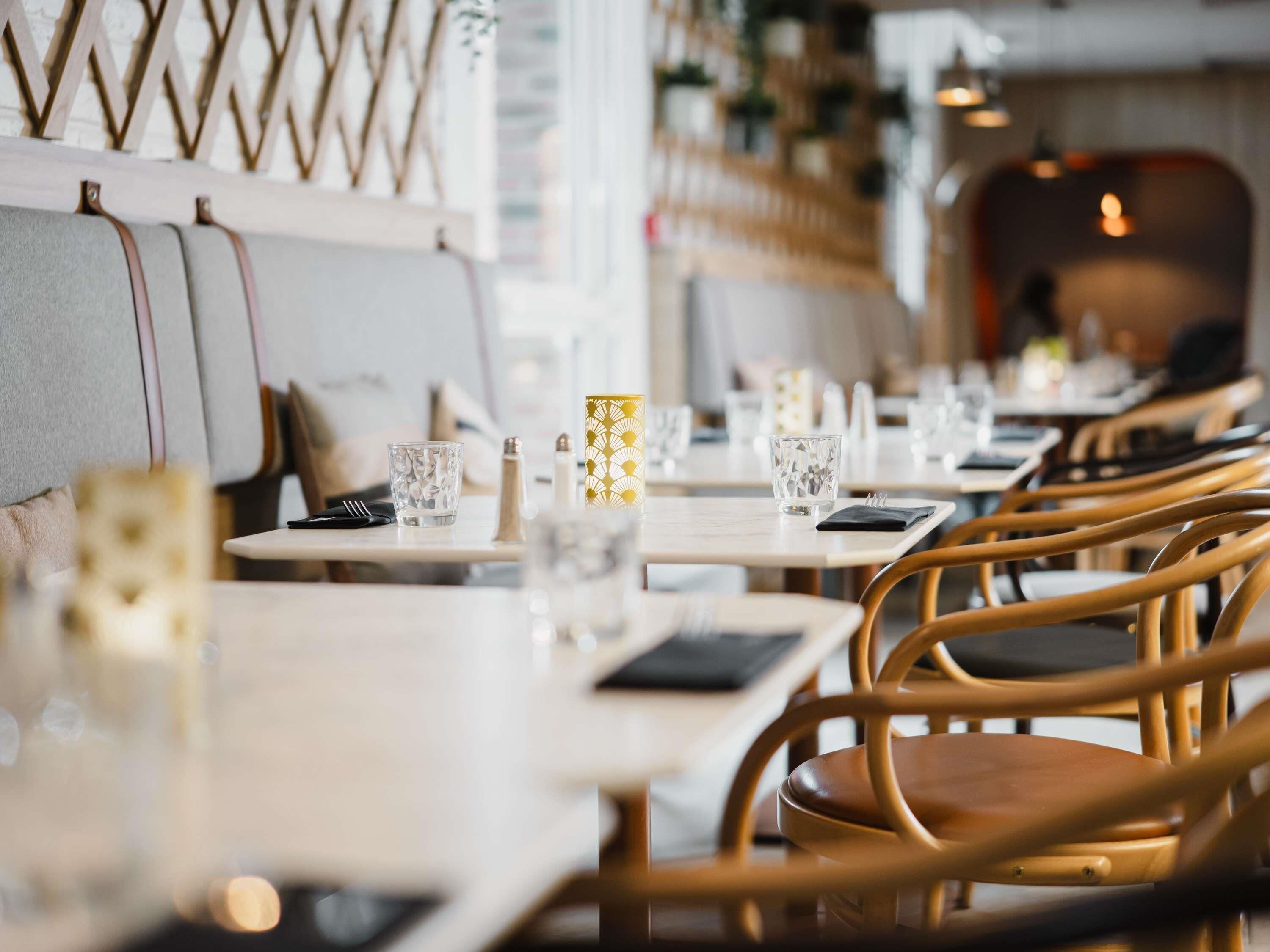 A restaurant with wooden chairs and tables, some with water glasses and napkins.
