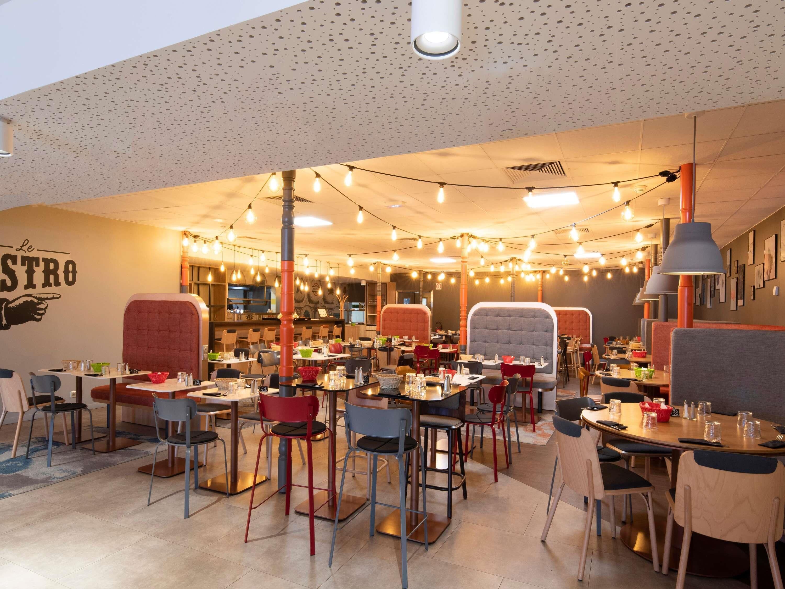 A restaurant interior with multiple dining tables and chairs, string lights, and a wall with a sign.