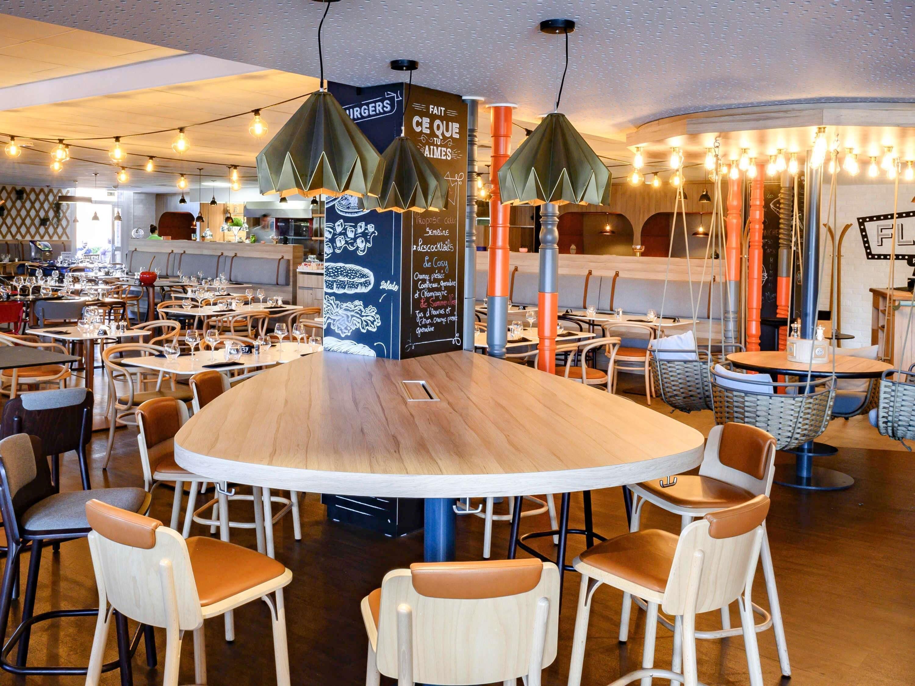 En restaurantindretning med runde borde, stole og hængende pendellamper.