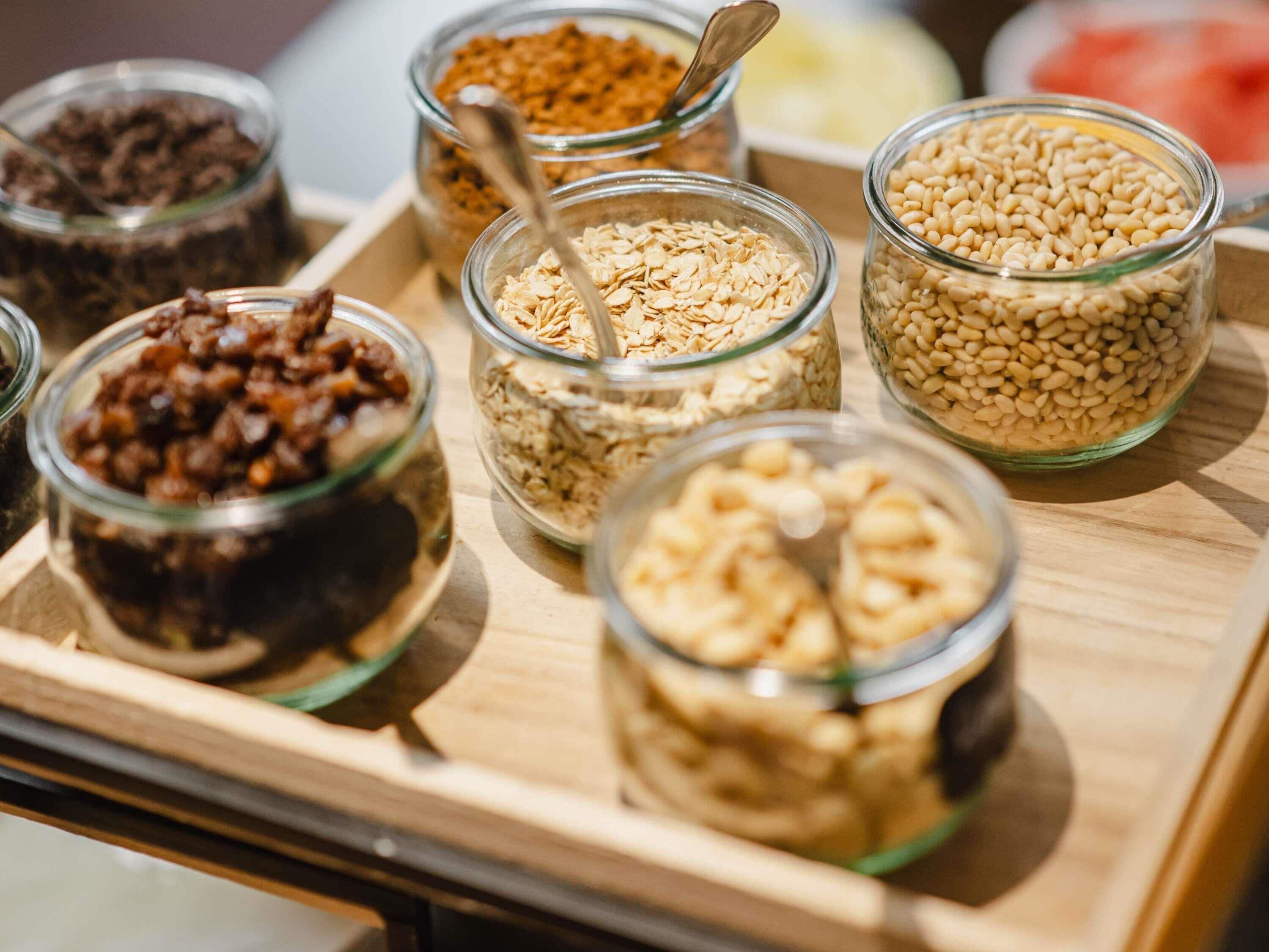 Un vassoio con diversi barattoli di vetro contenenti cereali e semi vari.