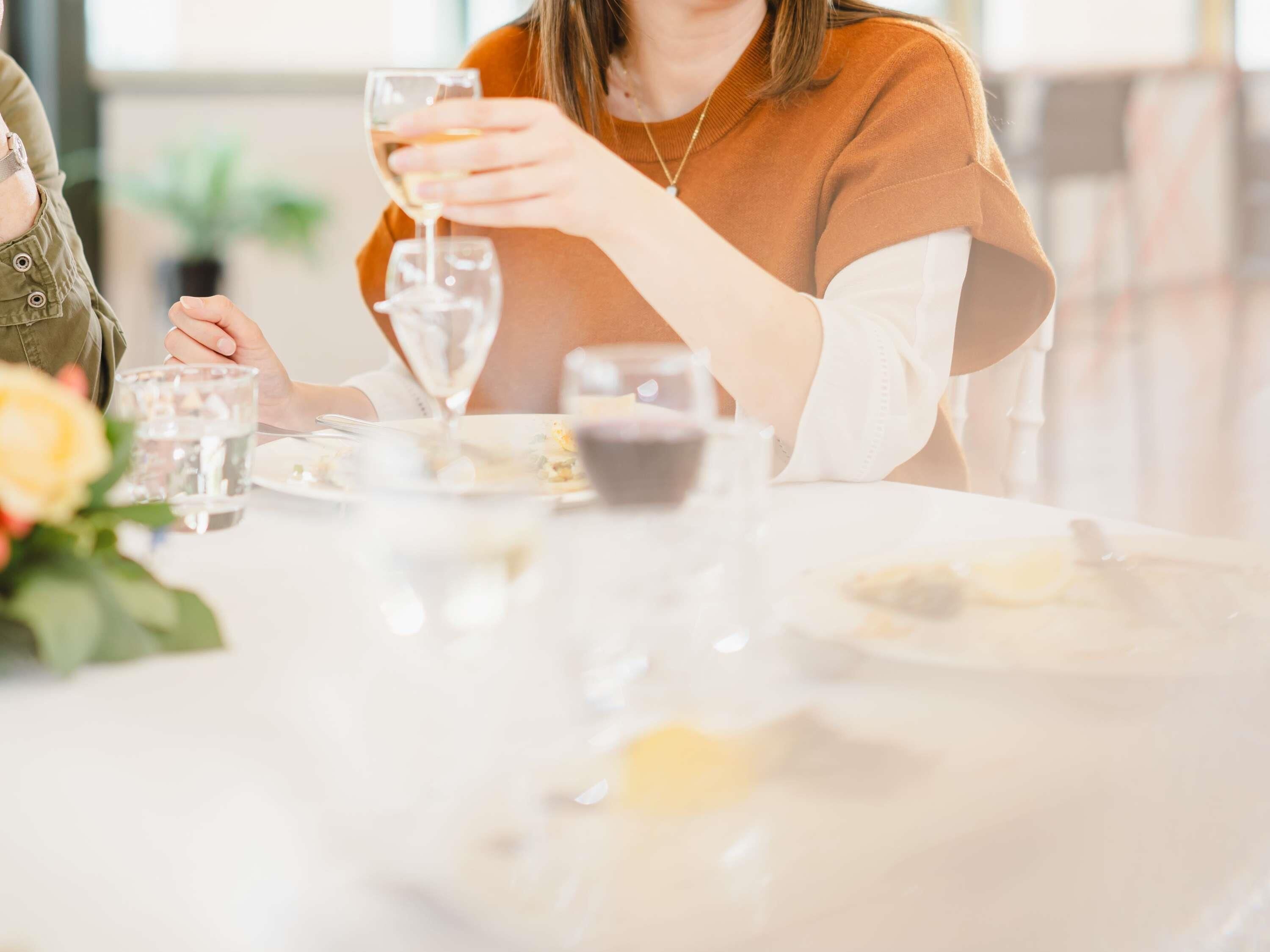 Una mesa de comedor con una copa de vino blanco, un vaso de agua y un plato de comida.