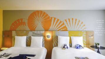 Habitación de hotel con dos camas, cabecera de madera con diseño de sol radiante, una mesita con una planta y una pared con una cita en francés.