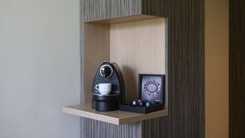 Una estantería con una cafetera, una taza y un expositor de cápsulas de café.