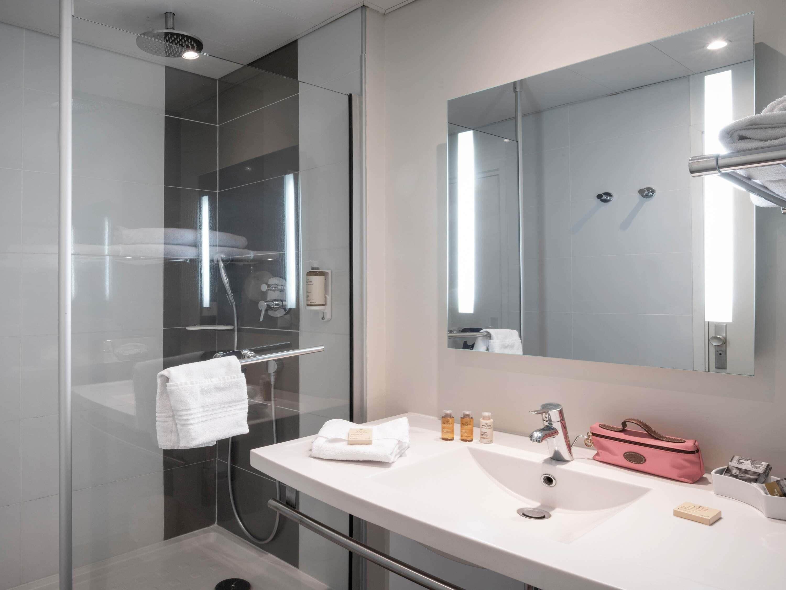 A modern bathroom with a glass-enclosed shower, a white sink, and a large mirror.